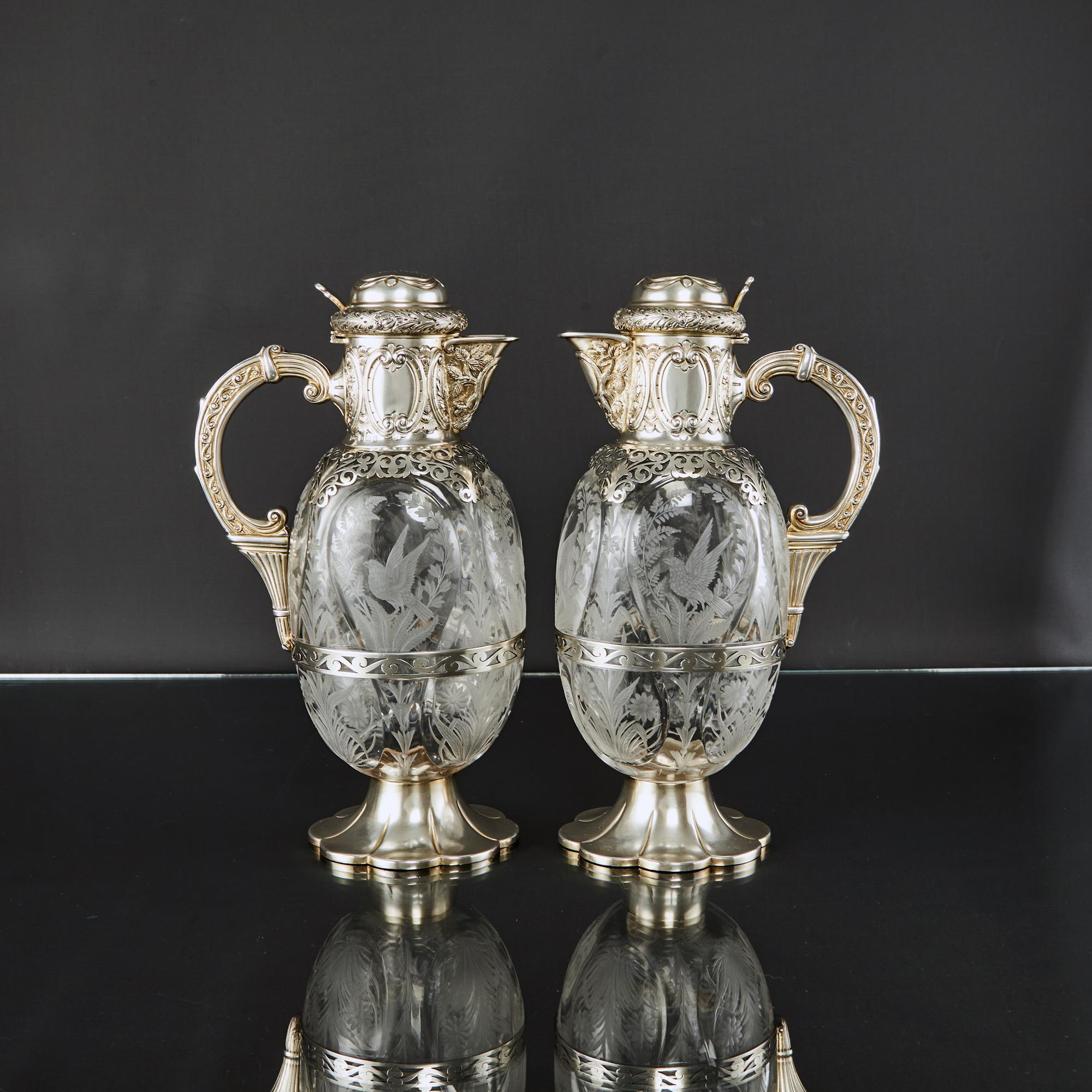 An excellent pair of antique Edwardian wine jugs of the finest quality. The ovoid glass bodies feature deeply cut panels, finely hand-engraved birds of prey surrounded by branches of bellflowers, ferns, foliage and flowers.

The silver mounts are
