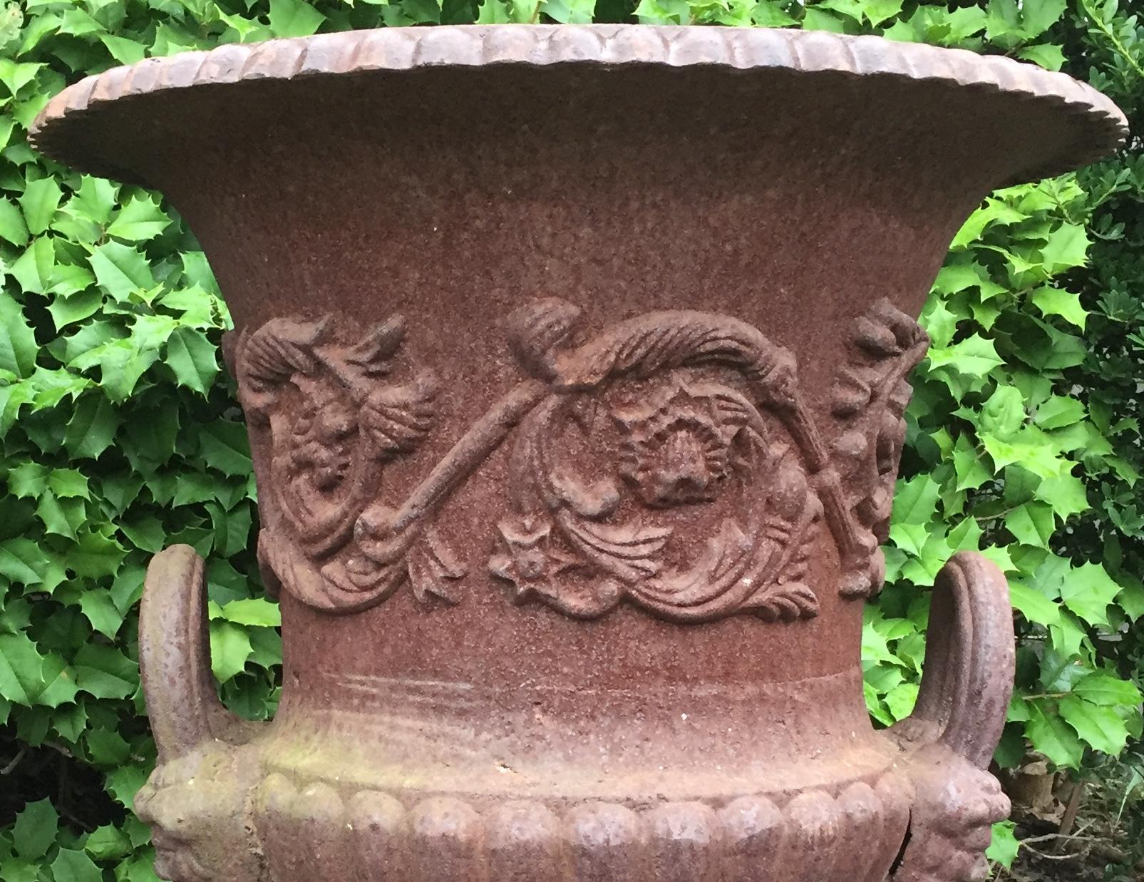 Very impressive pair of antique brown iron urns having ornate scrolly decoration and mythological faces as well as fluting around the bases. Found in England, circa 1860.