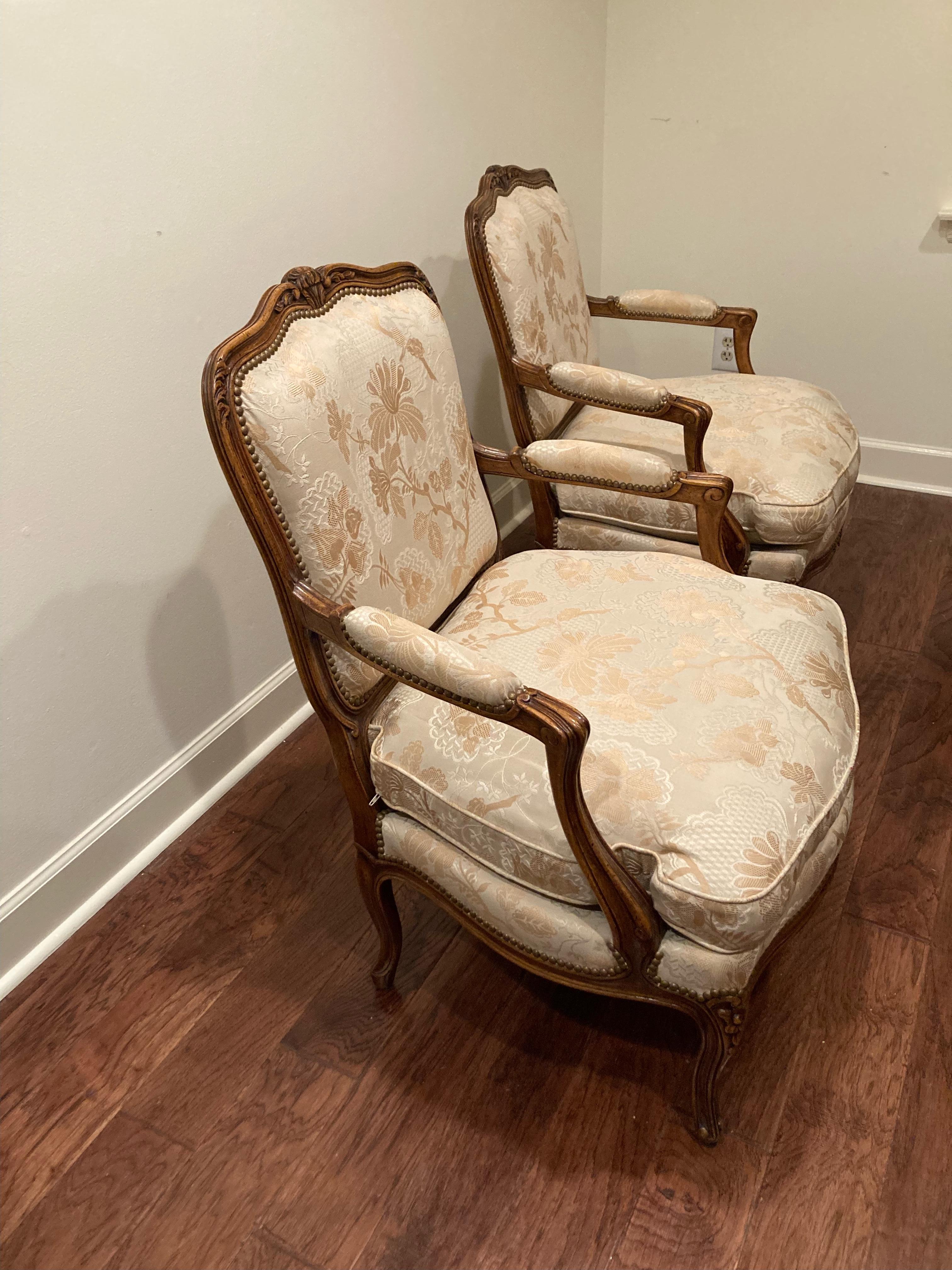 Elegant pair of classic Louis XV style fautueil armchairs having carved walnut frames and floral tonal creme and beige textured damask fabric. 
Seats are down filled. Style is almost identical to George Smith Louis bergeres but these are by high