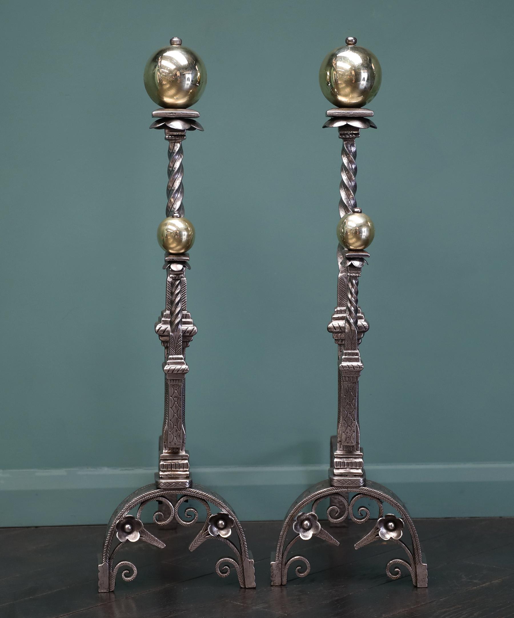 A magnificent pair of Italian polished brass & wrought fire dogs, andirons. The standards with twist, stepped-collars and detailed incising. All set on arched supports with inner trefoil and floral motifs. The brass ball finials sit over petals and