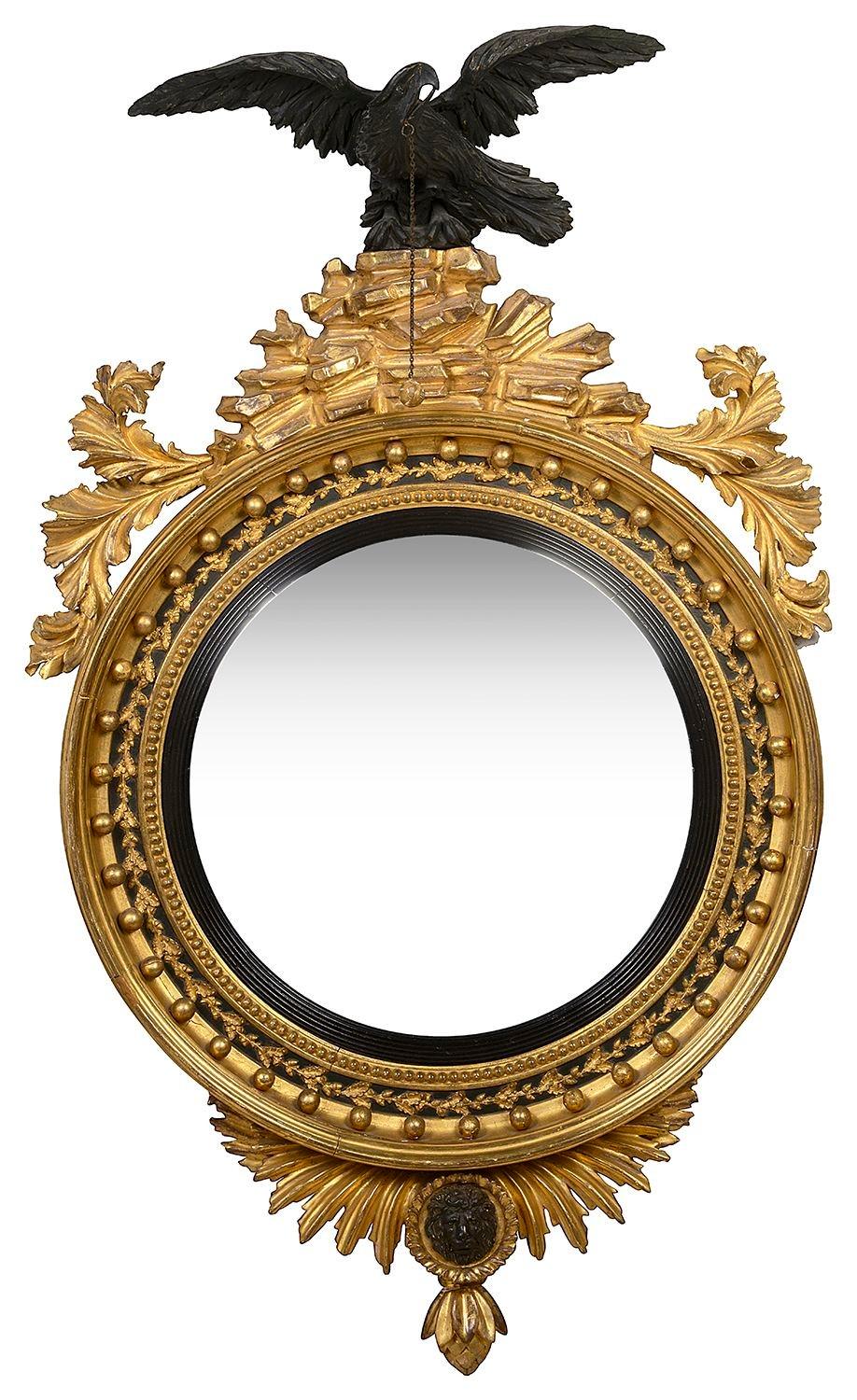 A magnificent pair of Regency period carved giltwood convex wall mirror, having ebonized eagles perched above the carved rocky outcrops, scrolling leaf decoration either side, inset gilded balls surrounding the ebonized reeded slip and the convex