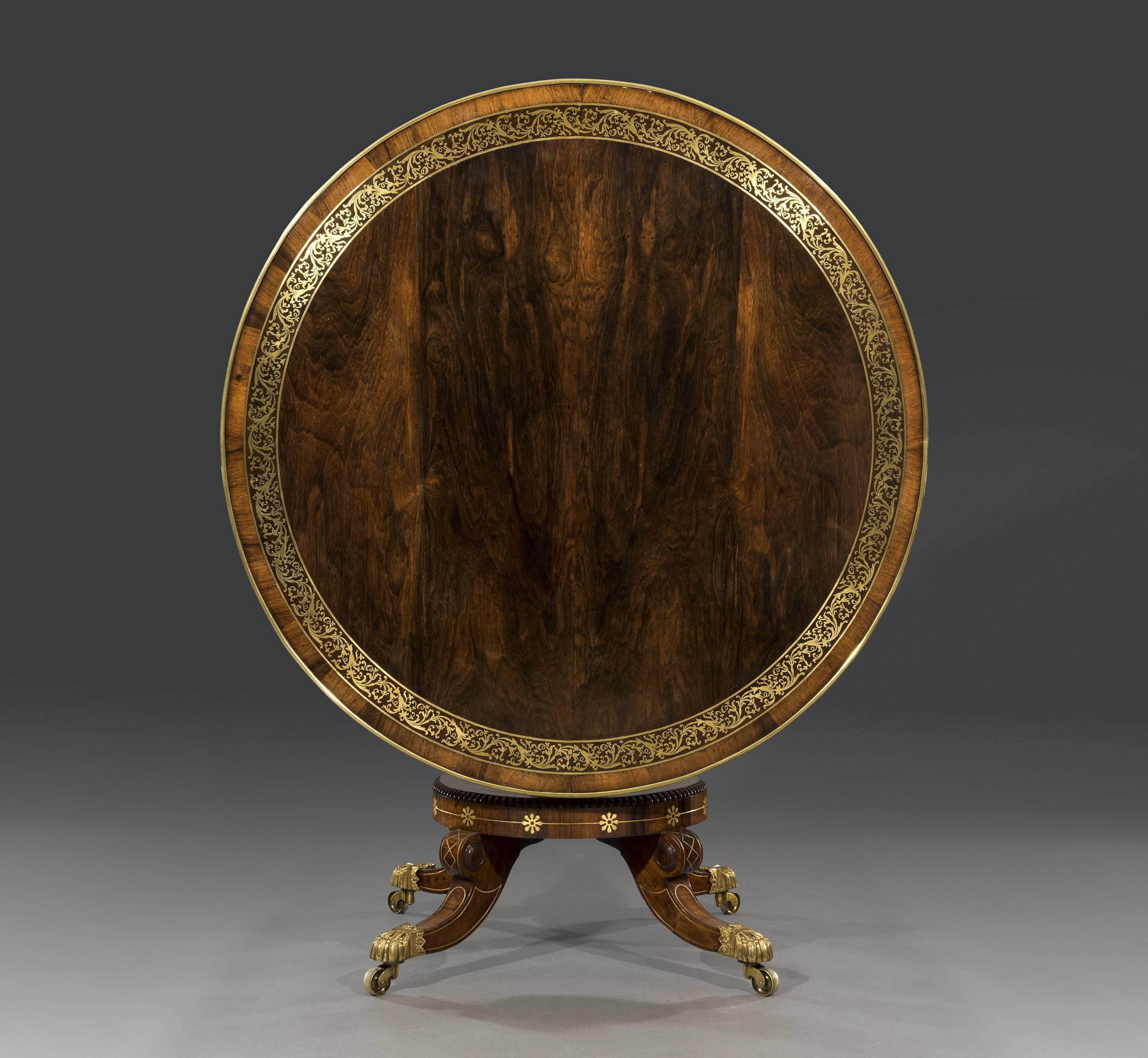 The book-matched rosewood circular veneered top is intricately inlaid in brass with rosewood crossbanding and gilt brass moulding with a neoclassical motif to the top edge and a gilt brass trim to the bottom edge of the shallow rosewood frieze. This