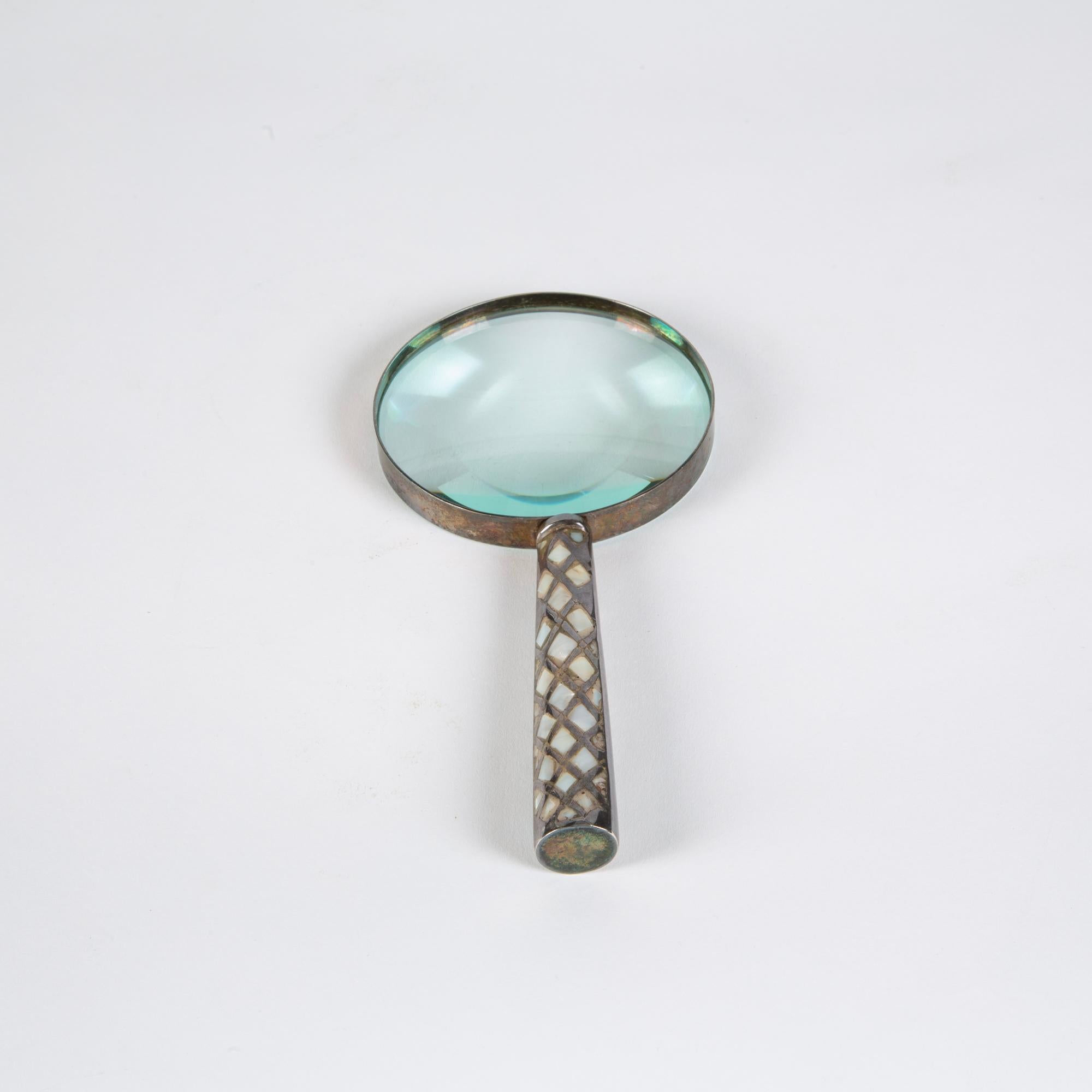 Patinated silver metal frame magnifying glass. The handle features a geometric pattern of inlaid mother of pearl. It is a great finishing piece in your library or fun coffee table décor.

Dimensions: 9?