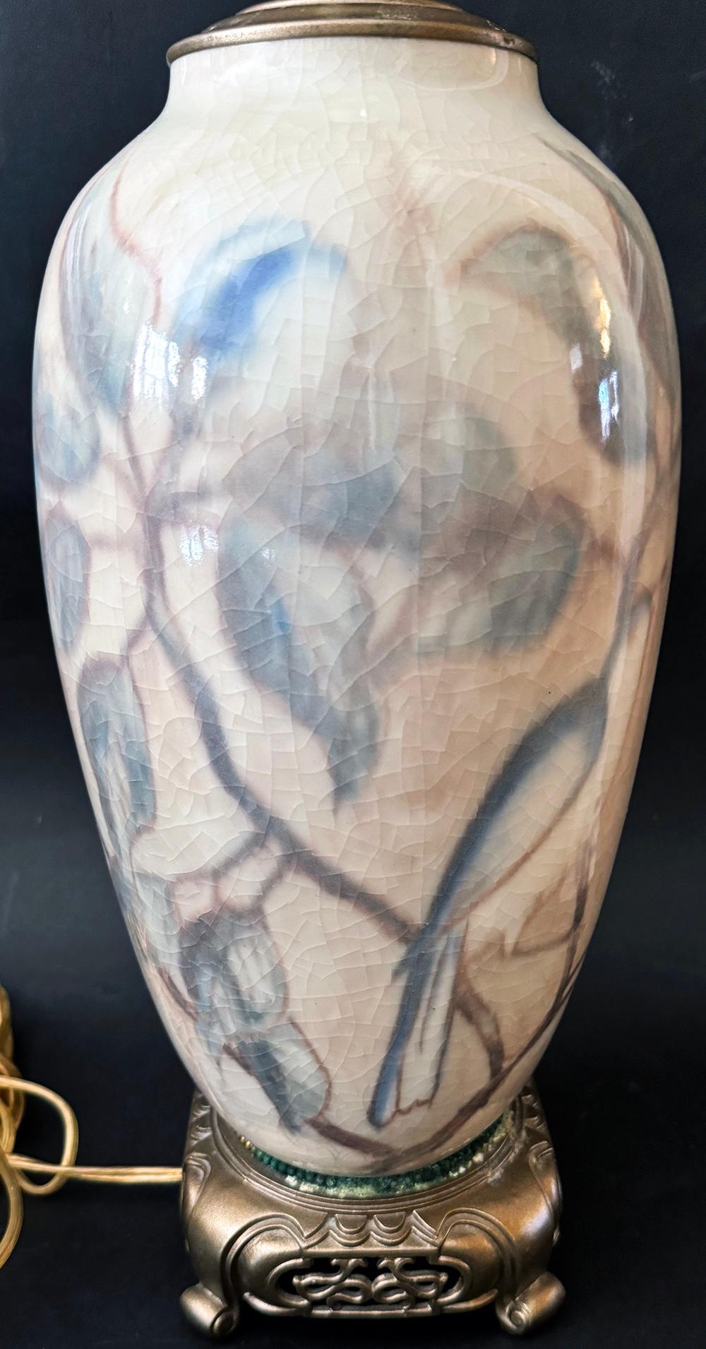 Beautifully glazed in tones of blue, gray, white and tan, this unique lamp base by the famed Rookwood company in Cincinnati features a series of magnolia branches laden with flowers, accompanied by several blue birds.  The glaze has a misty, soft