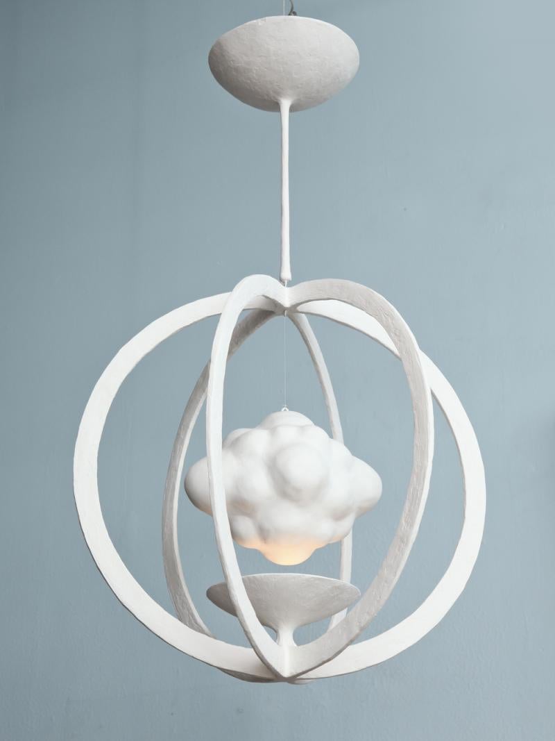 Surrealist-inspired pendant of plaster over metal. Gyroscopic form surrounds a shallow dish which illuminates a floating cloud. This fixture comes outfitted with one 2-pin G9 socket, suitable for halogen or LED bulbs. Made per order in France and