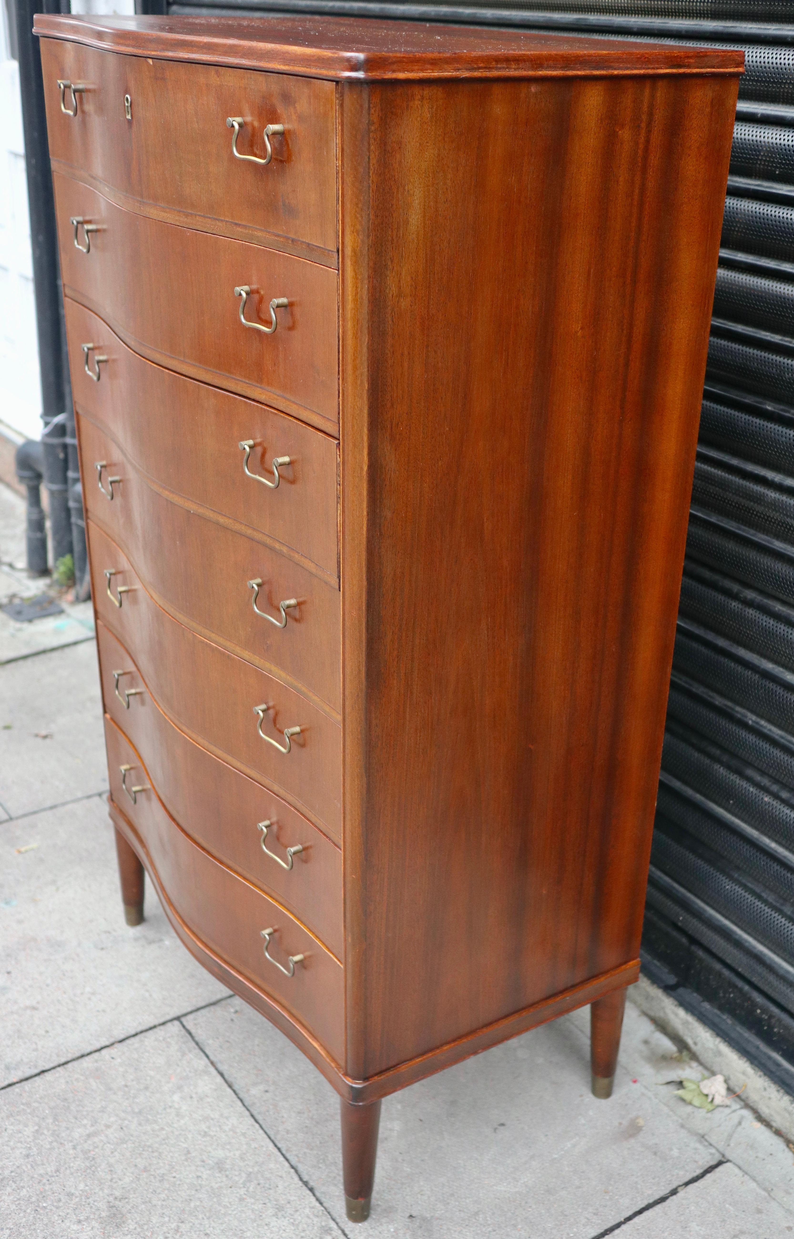 A vintage 1950s mahogany veneered serpentine fronted,  seven drawer 'tall boy' chest of drawers on a solid mahogany base with brass fittings.  This piece is fitted with brass handles and is in good vintage condition, when you consider it's age. It
