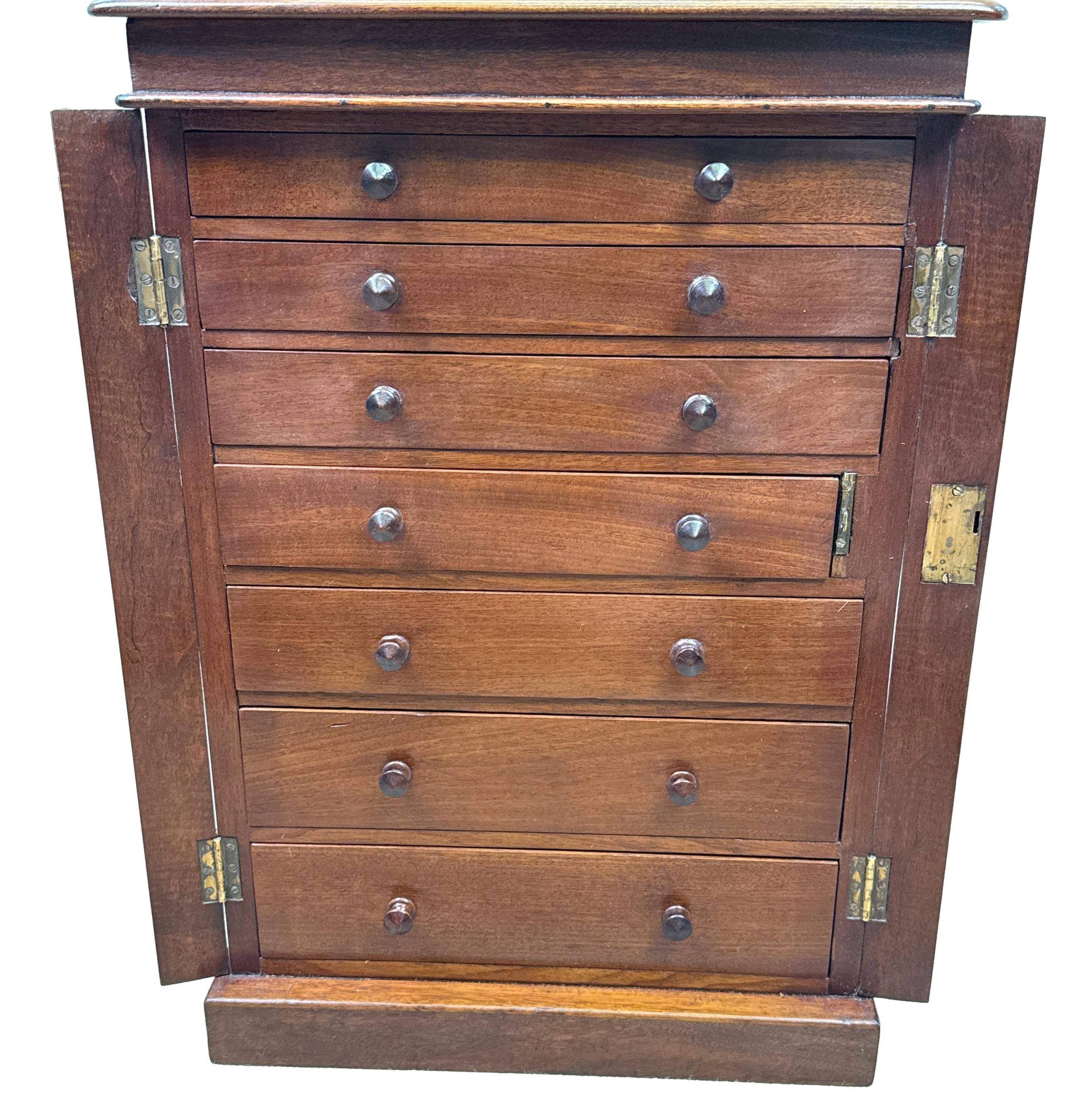 Atractiva cómoda Wellington de caoba de finales del siglo XIX, en miniatura o para niños, con tapa rectangular y siete cajones con pomos de madera torneada originales, rodeados de pilastras con bisagras y elevados sobre un zócalo original. 

Las