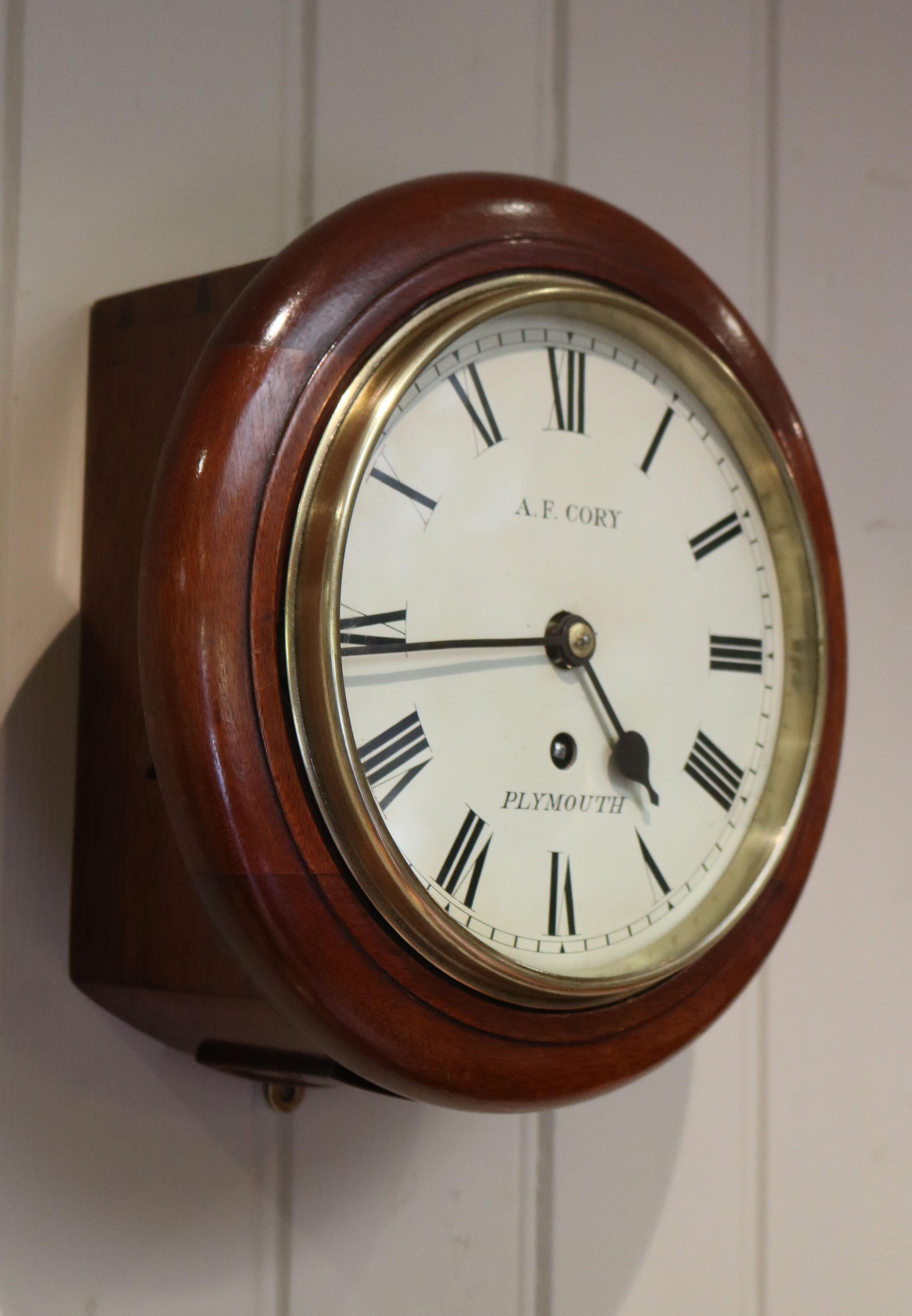 A solid mahogany cased 8 inch diameter dial clock. It has a traditional pegged case, a turned outer rim, a brass bezel and a painted enamel dial signed by the retailer A F Corey of Plymouth. The chain driven 8 day fusee movement has stopwork to