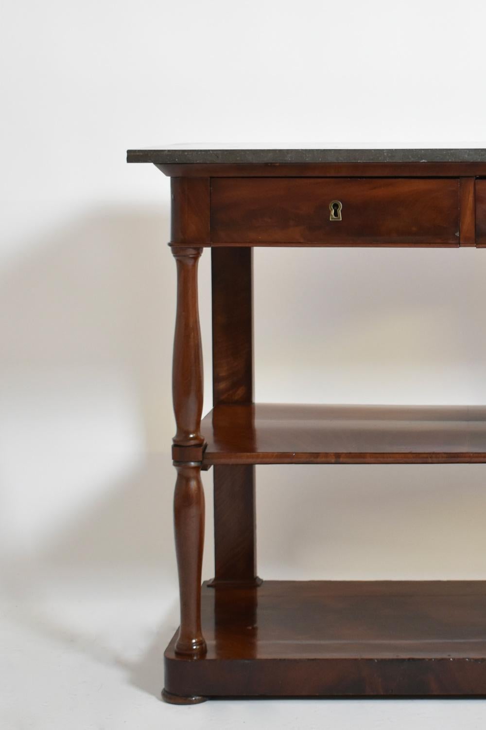 Consolle in mogano impiallacciato apribile con due cassetti nella fascia e due vassoi nella parte inferiore. Piano in marmo, montanti a doppio binario. Francia, XIX secolo.