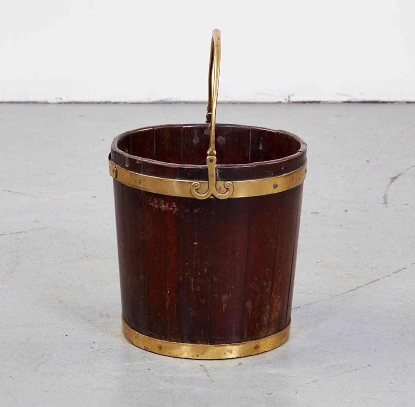 An early 19th century mahogany bucket bound by two brass bands. Heavy brass handle with decorative ram's head brass hinges. Coopered and staved construction. Well patinated. Originally used to store turf or peat, and now useful as a kindling bucket,