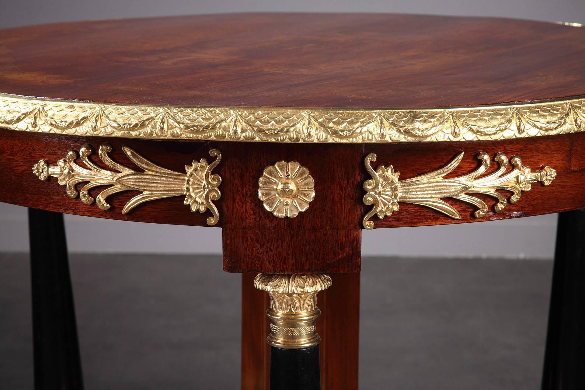 Mahogany and gilt bronze gueridon table resting on a central foot above a tripod base, surmounted by three dark wood columns decorated with gilt bronze Corinthian capitals and sphinx. The tray in wood marquetry with floral decoration and ormolu