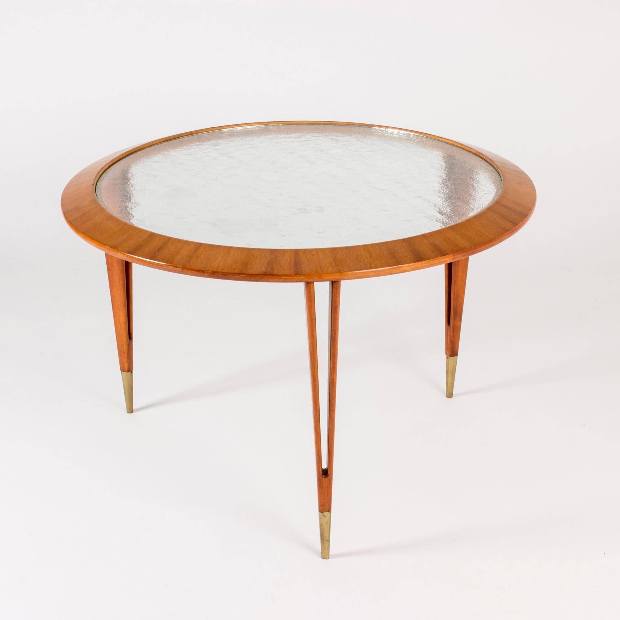 Beautiful coffee table by Bertil Fridhagen, with a glass table top in a mahogany frame. The mahogany veneer is layed in a pattern of rays from the center. Legs sculpted in a split design with brass feet.