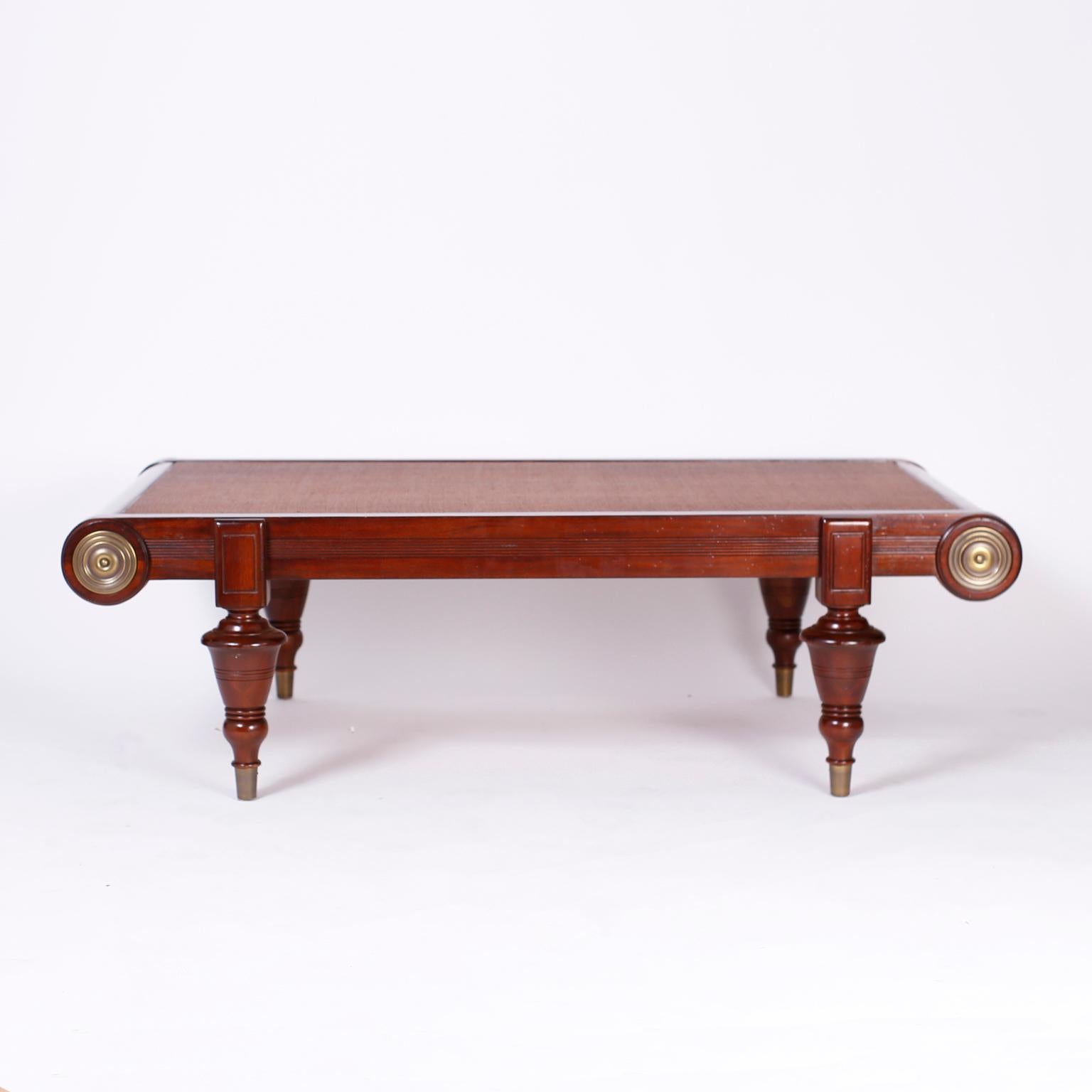 British colonial style coffee table with a grasscloth top and a mahogany frame with brass medallions designed with 19th century influences, bold turned legs, and brass feet.