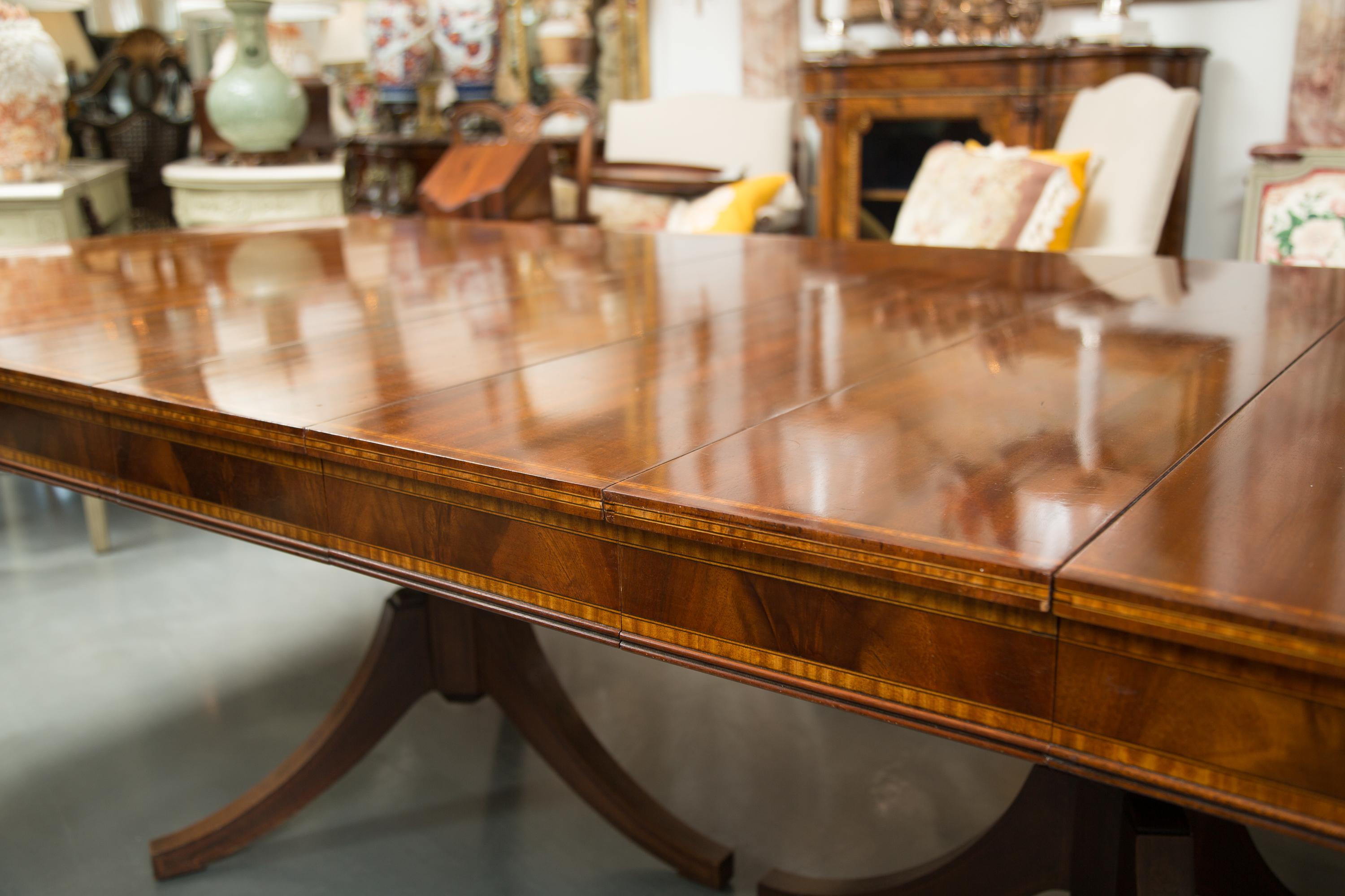 This is a very pleasant inlaid mahogany dining table with four additional leaves for extension. The top has a straight edge and is positioned over a prominent inlaid frieze. The table is supported by two baluster fluted pedestals, terminating each
