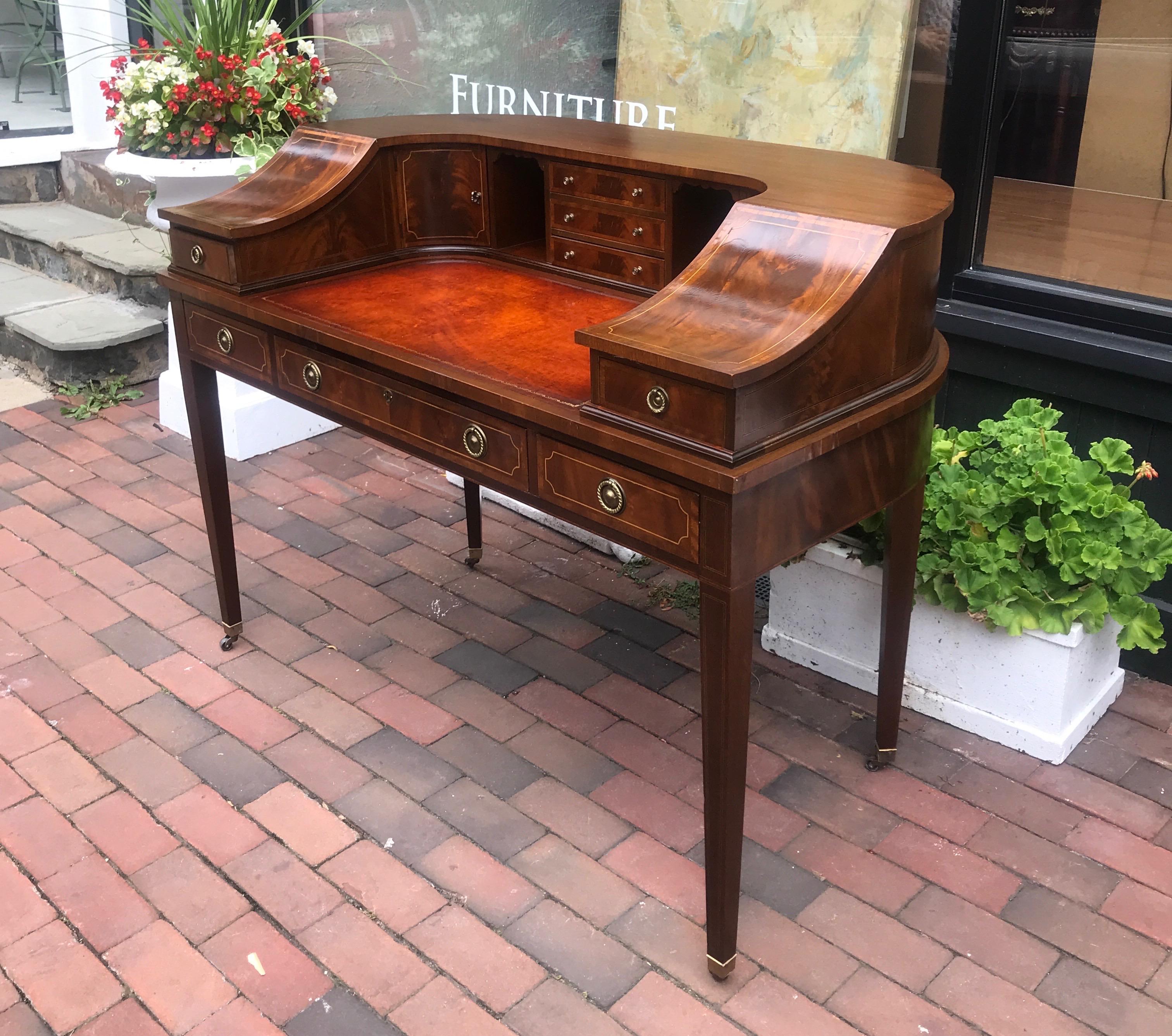 Elegant and formal flame mahogany Carlton house desk with leather writing surface. The desk with curved back and upper compartments with drawers and pigeon hole spaces. The writing surface in leather with three drawers along the front apron. Resting