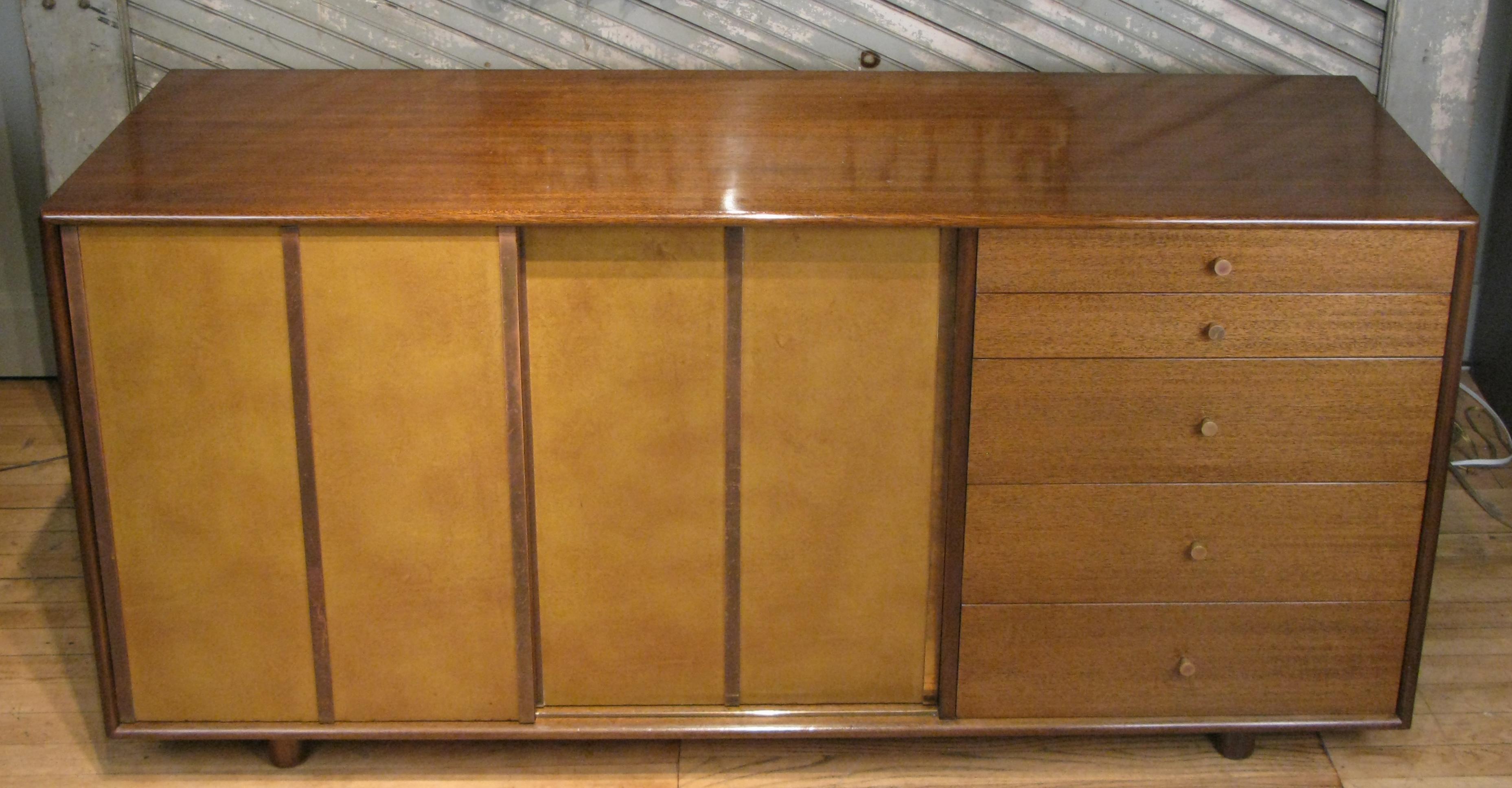 A very handsome 1950s cabinet chest designed by Harvey Probber, with a mahogany case and sliding leather doors covered in leather and brass trim. The sliding doors conceal shelves on the left and slide out mahogany trays on the right. The right side