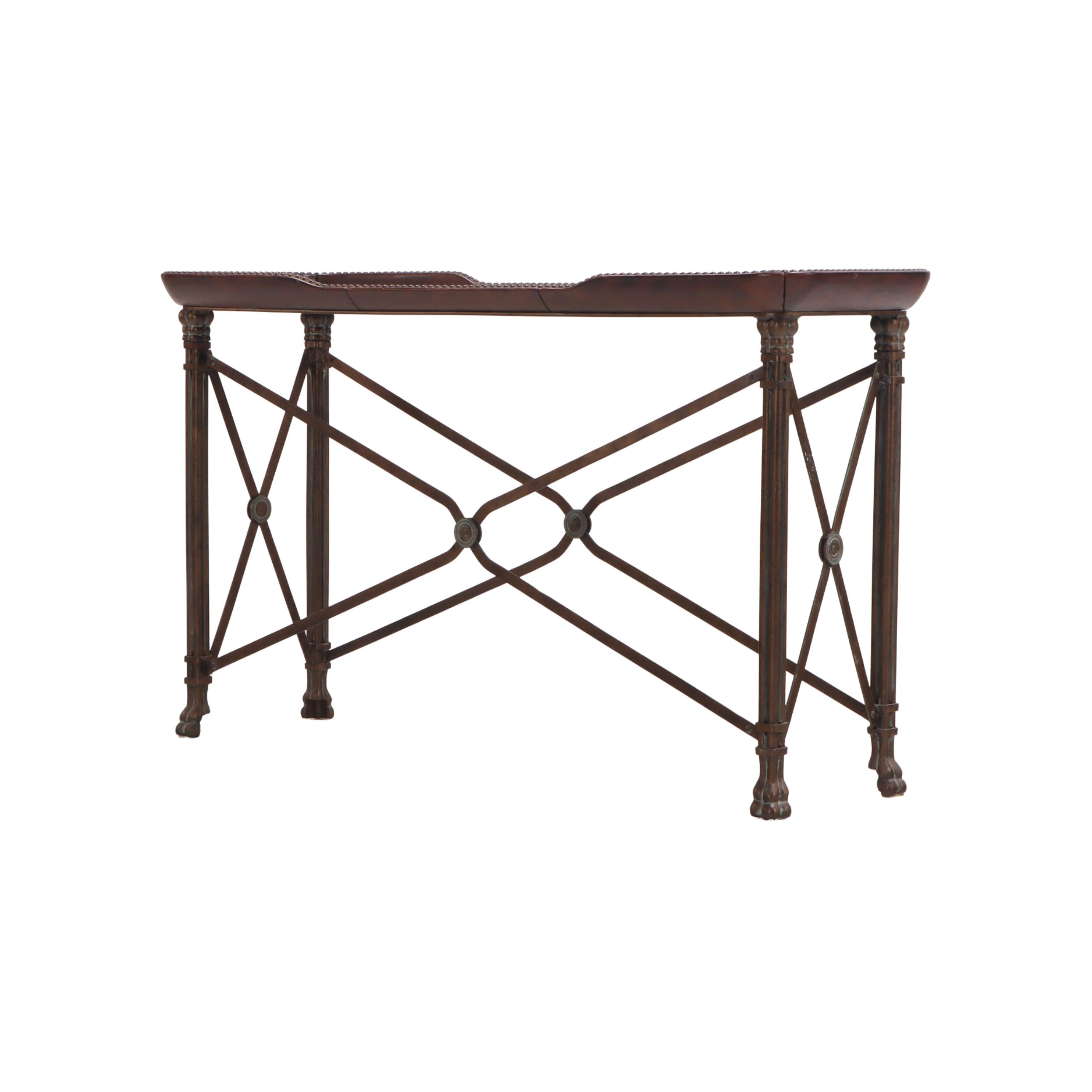 Esta consola de estilo neoclásico tiene un tablero de caoba forrado de cuero con detalles de tachuelas con cabeza de clavo. En la base del tablero hay una losa de mármol verde con bordes redondeados. La base de la mesa es de latón, con camillas en