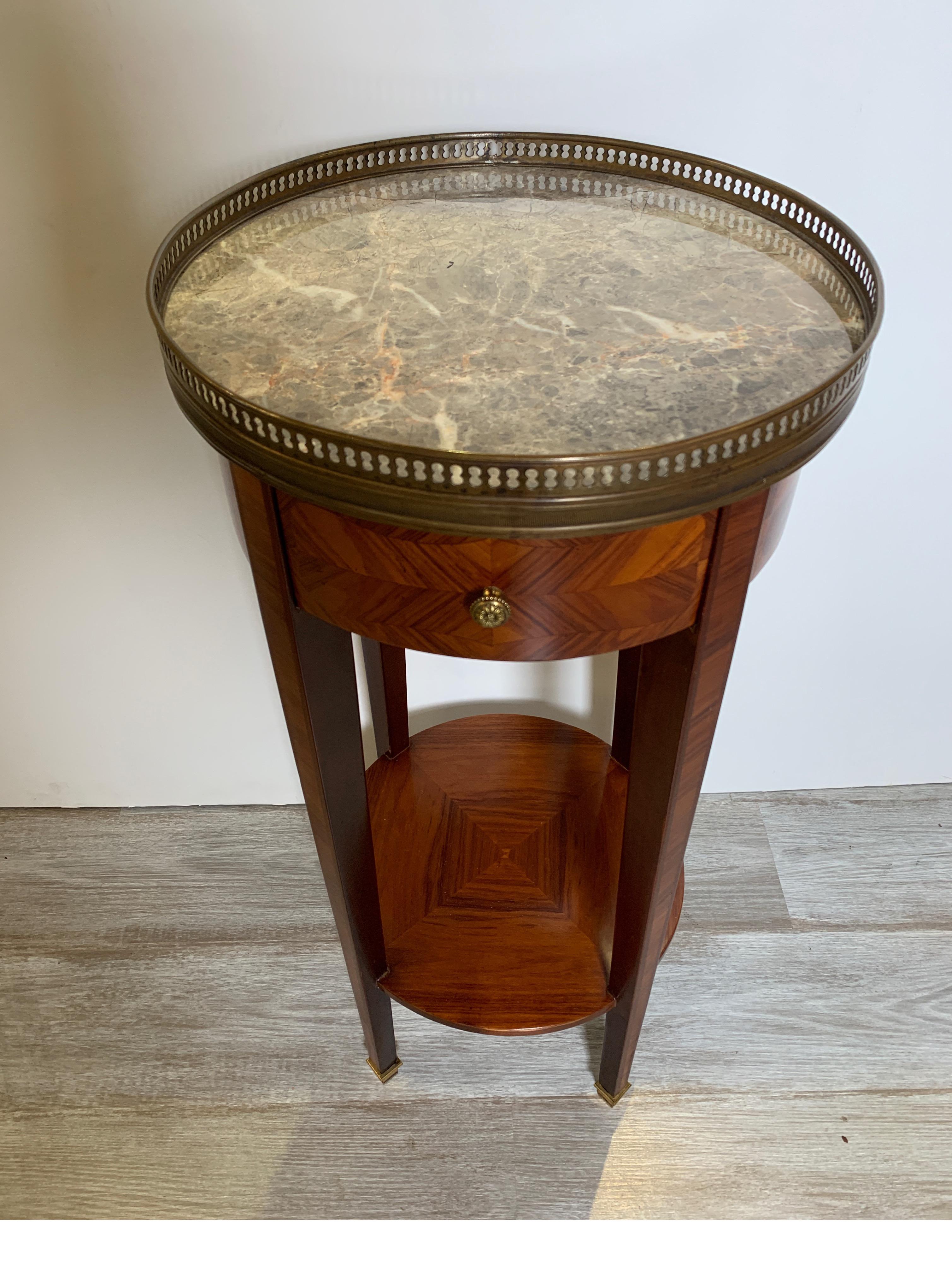 Diminutive round mahogany table with brass gallery edge and marble top Louis XVI style. The top resting on four tapering legs with lower shelf. Elegant neoclassical style.