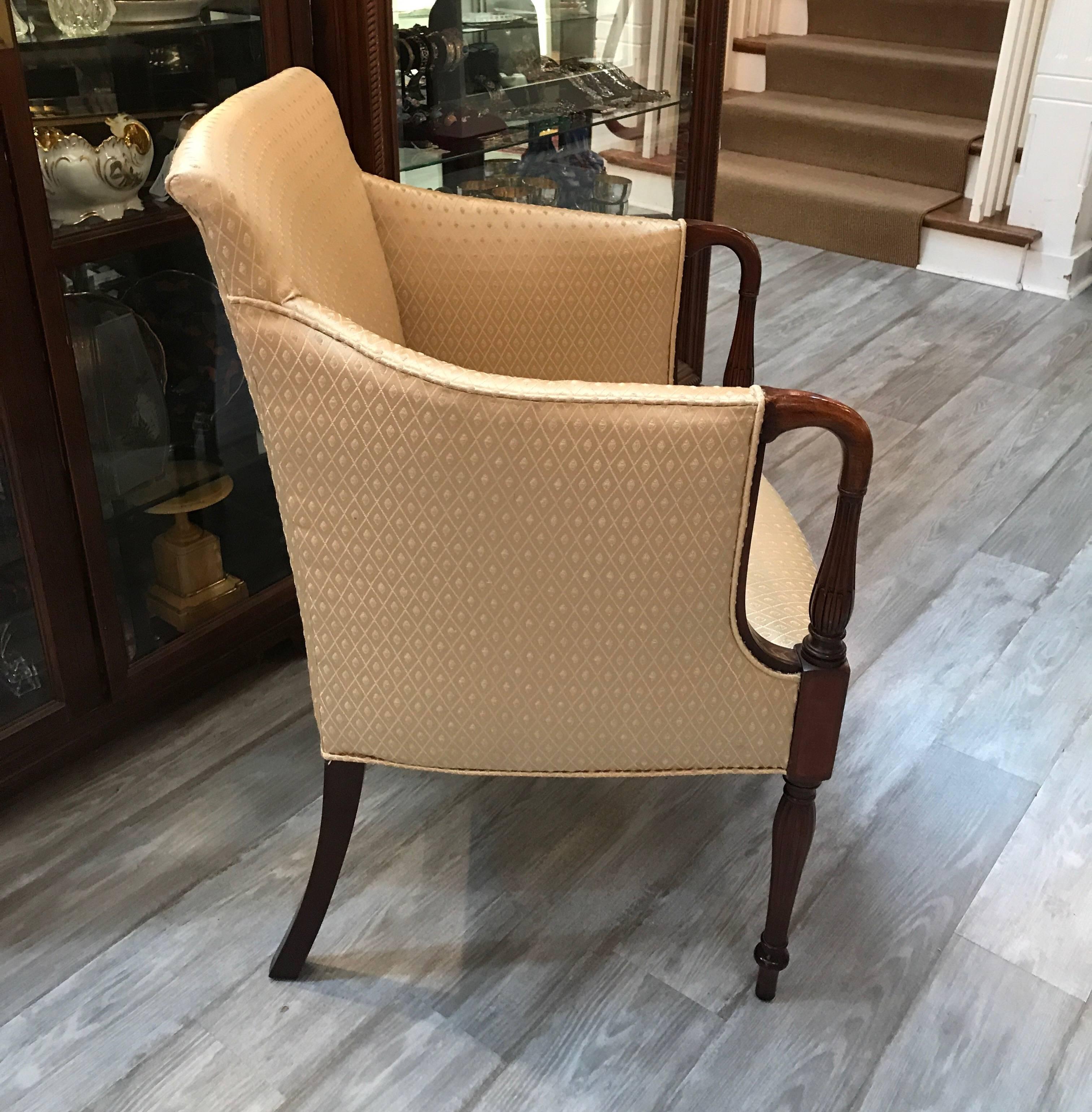 A diminutive Sheraton style mahogany occasional chair with new fabric. The attached back and seat with turned arms, delicate inlay at the arms with turned and reeded legs. Perfect smaller accent chair.