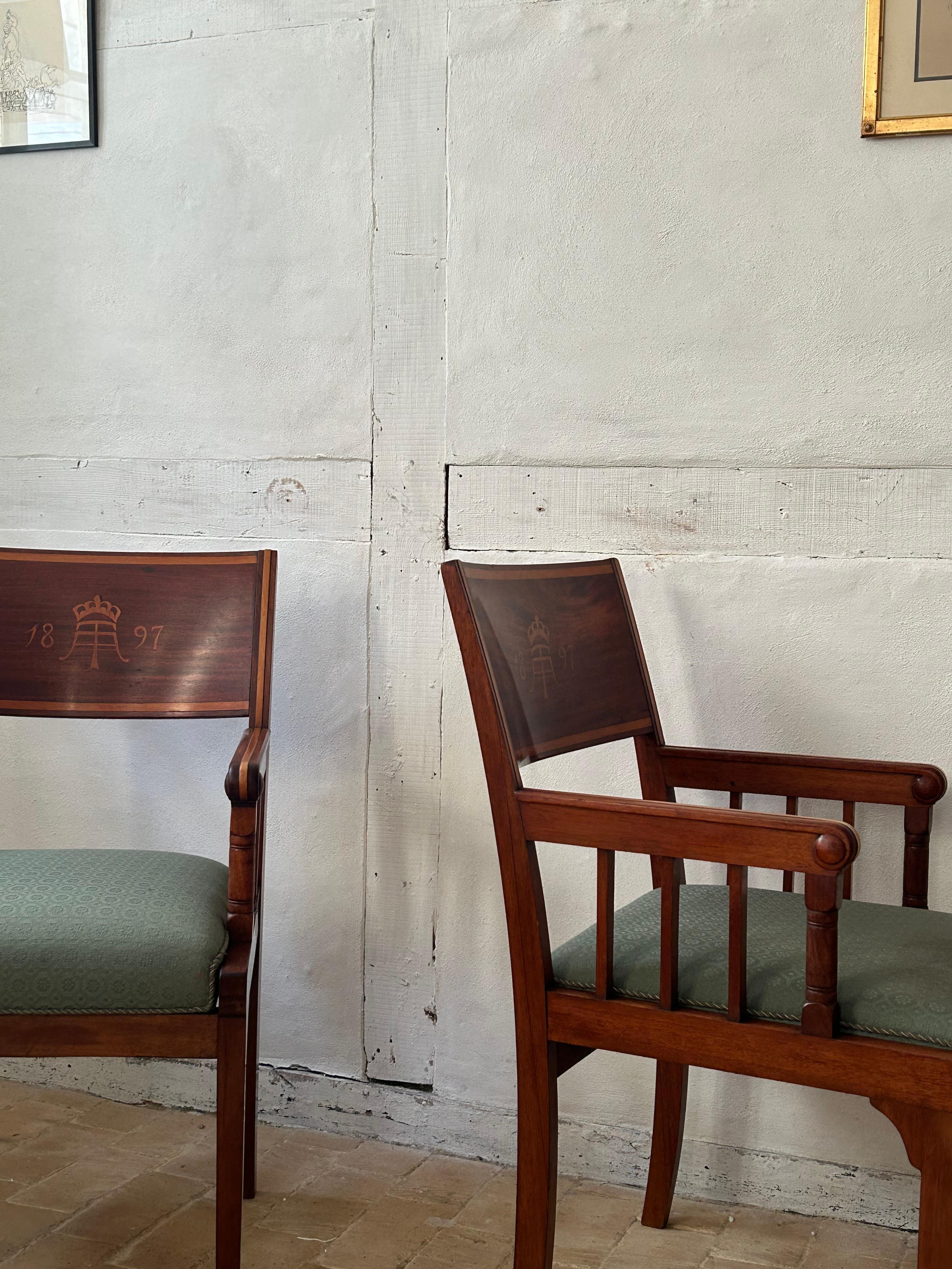 Cette élégante paire de fauteuils présente des cadres en acajou finement travaillés, ornés d'incrustations de bois d'érable. Les écussons sont incrustés du monogramme couronné de la douane d'Aarhus et de l'année 1897, ce qui souligne leur importance
