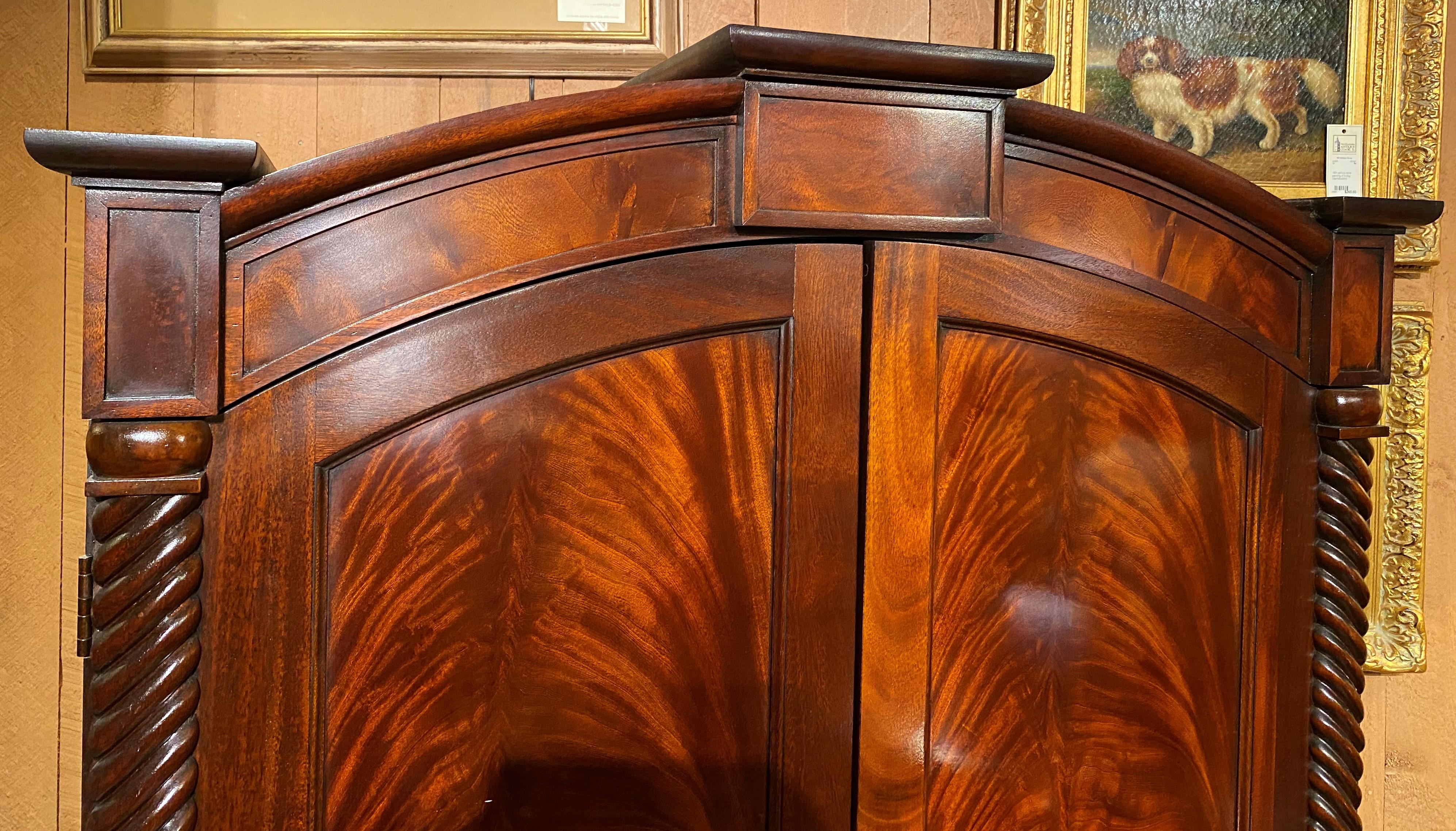 A fine mahogany arched top banded armoire with two doors, opening to a fitted interior with an open upper half with cutout back, probably used as an entertainment center with television, over two center fitted drawers, over two flame mahogany