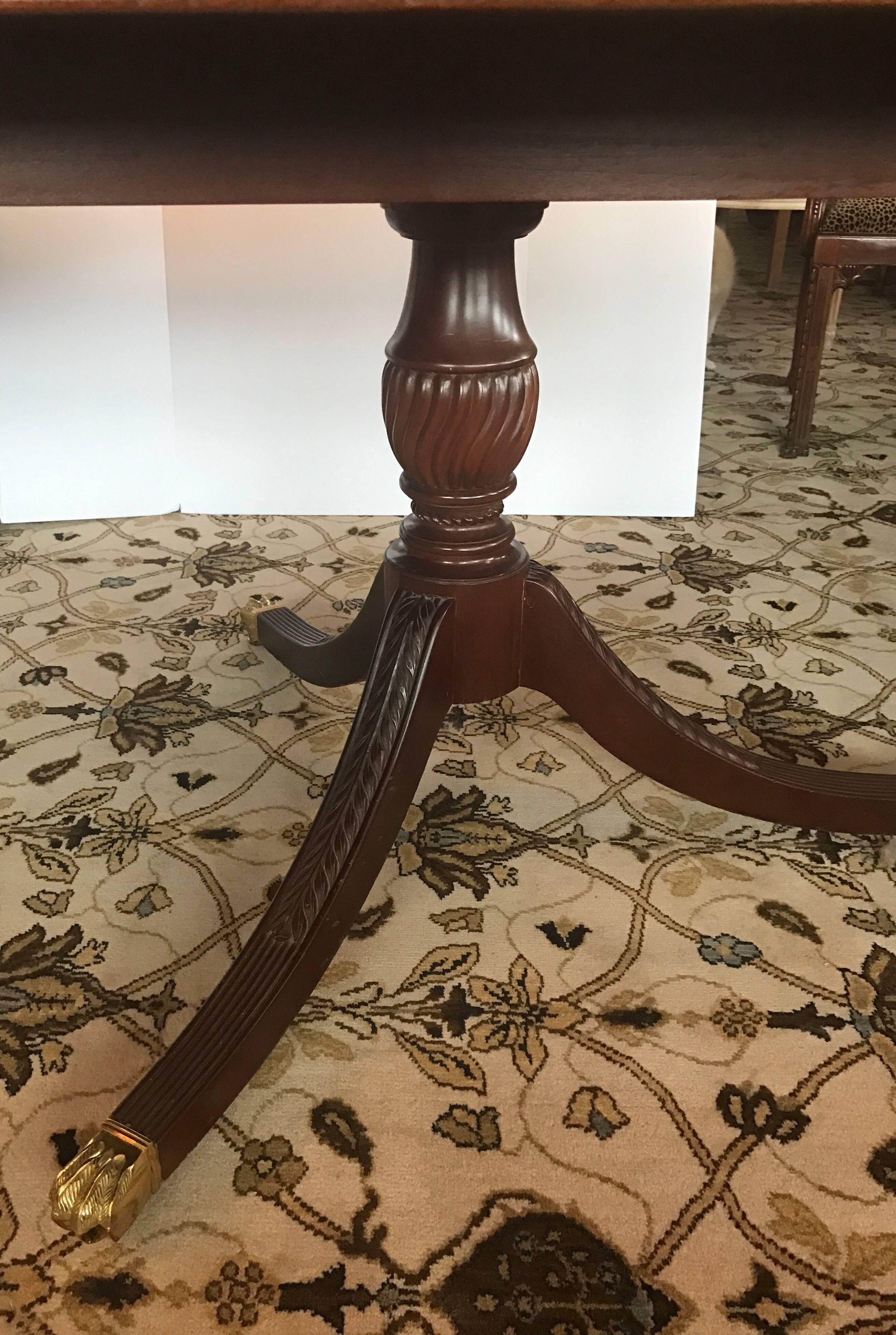 Magnificent English double pedestal dining room table with banded satinwood inlay around perimeter and brass lion feet on carved double pedestals. Table is shown with one leaf which seats ten. When both leaves are in, 12 fit comfortably. Each leaf