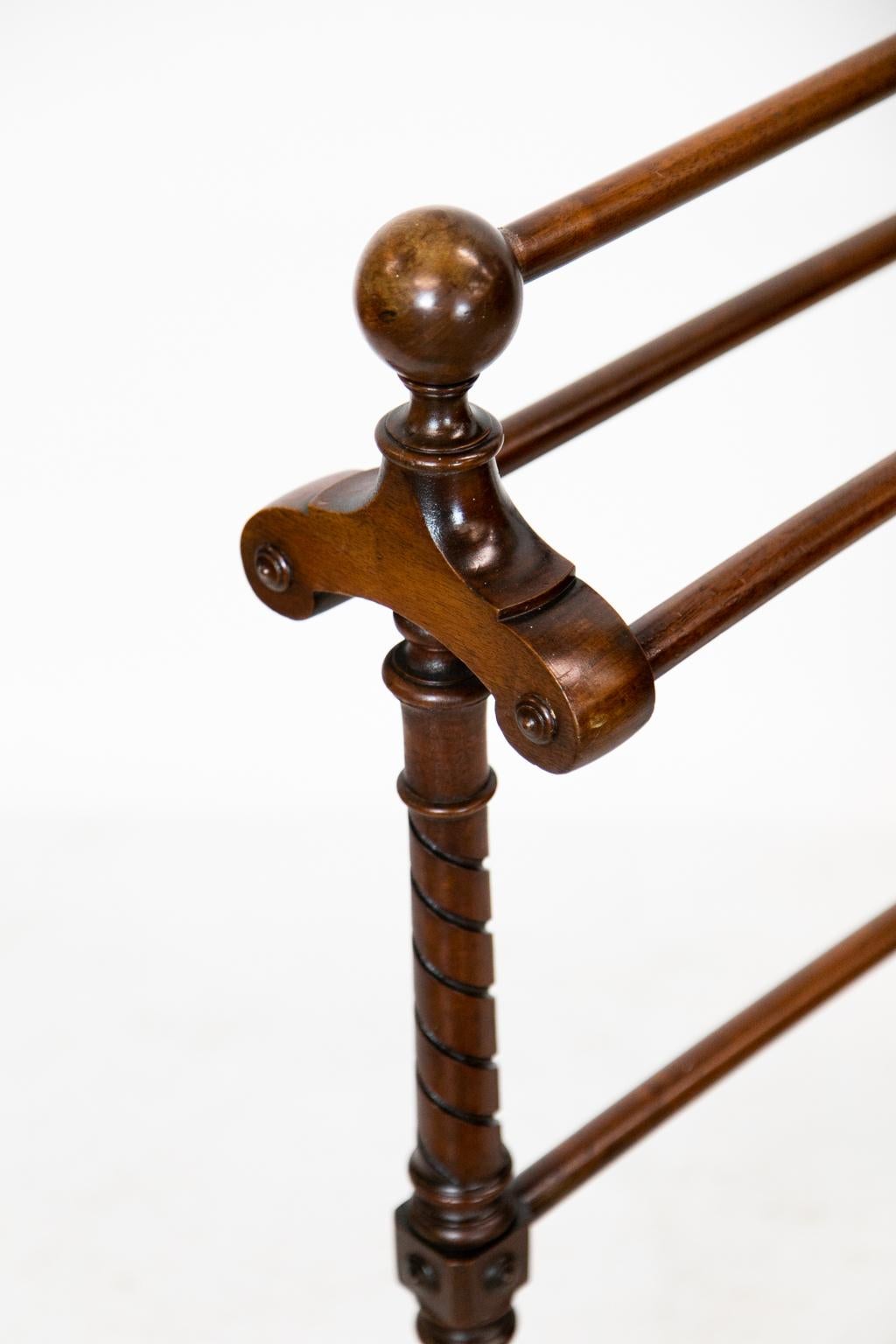 This mahogany blanket or towel rack has four rails. The top rail is supported by ends having cannon ball finials. The leg supports have carved spiral turnings that terminate in splayed legs which are connected by a double spiral turned stretcher.