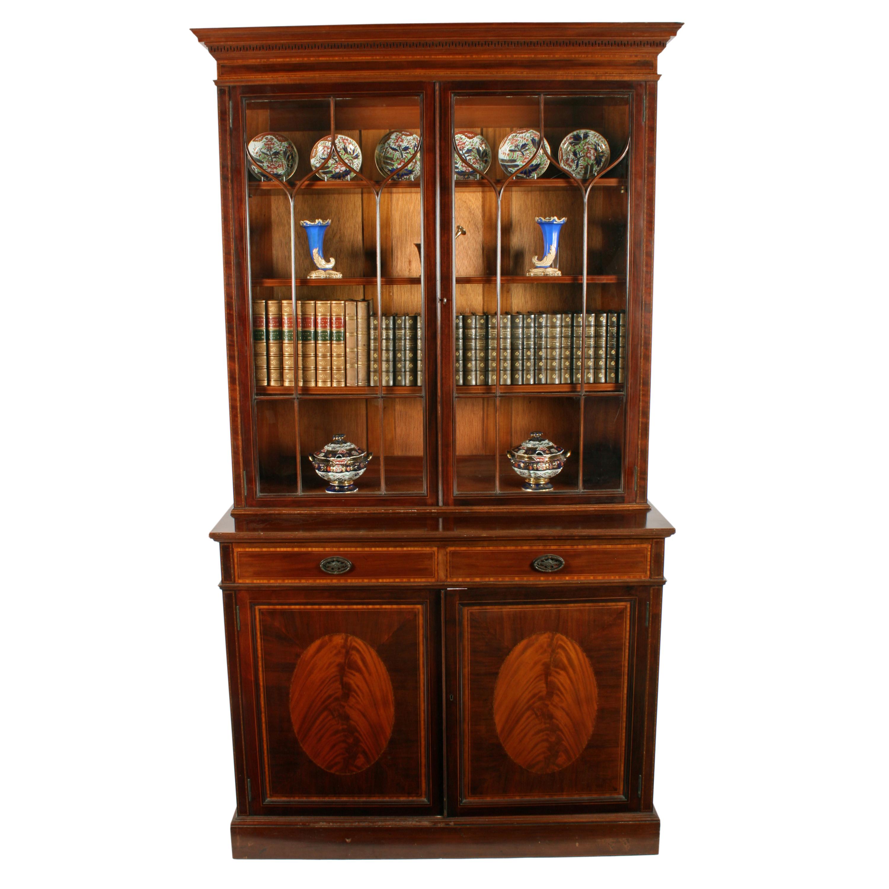 An early 20th century mahogany Sheraton style bookcase by Waring & Gillows.

The bookcase has an astragal glazed two-door cabinet top with three adjustable mahogany shelves.

The base has a pair of recessed panel doors with oval panels of flamed
