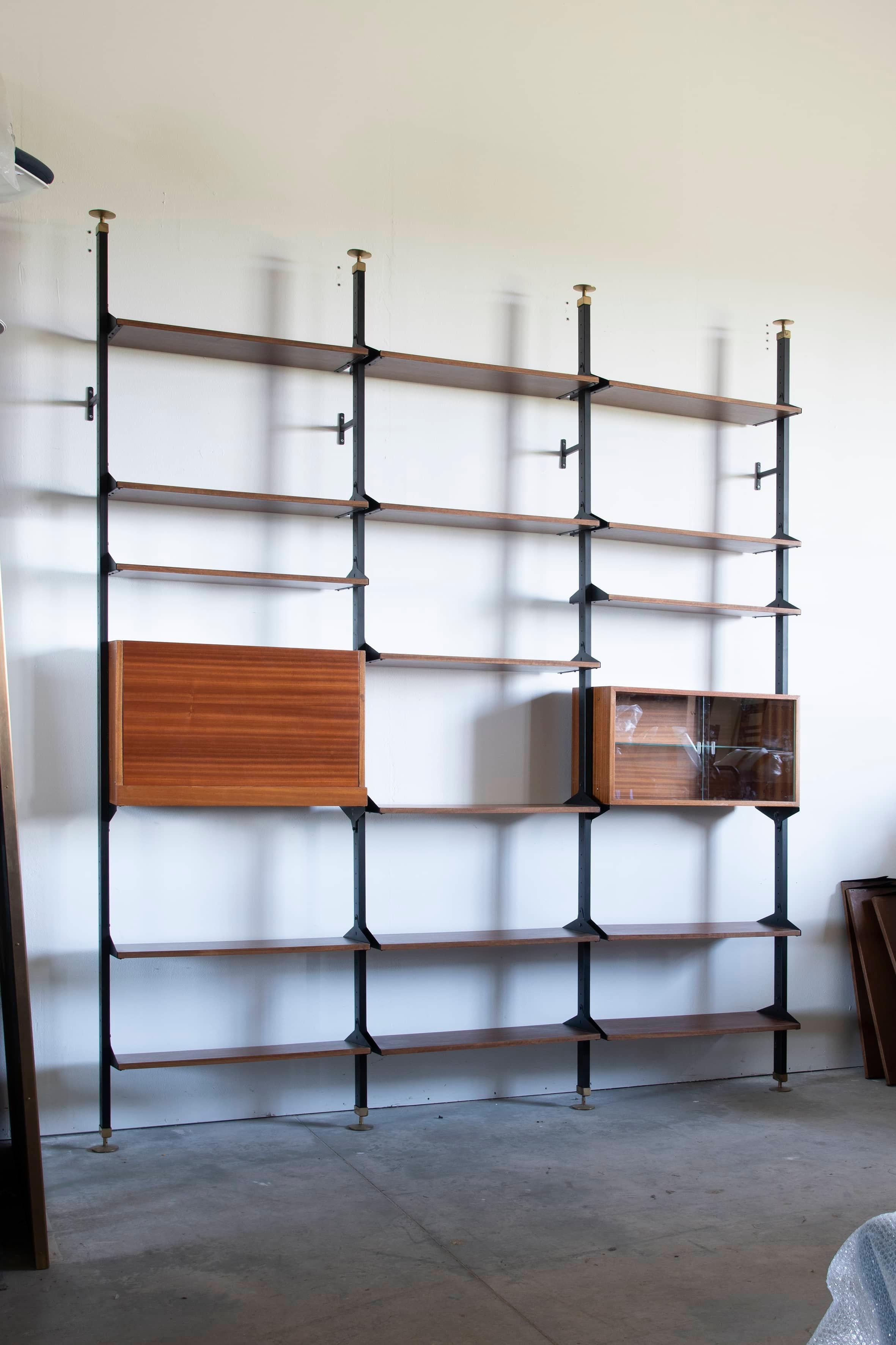 Mahogany bookcase with metal uprights and shelves Italy 1950s. The bookcase consists of four uprights and three modules organized with adjustable shelves and two storage compartments, one of which is open with sliding glass doors and one with a