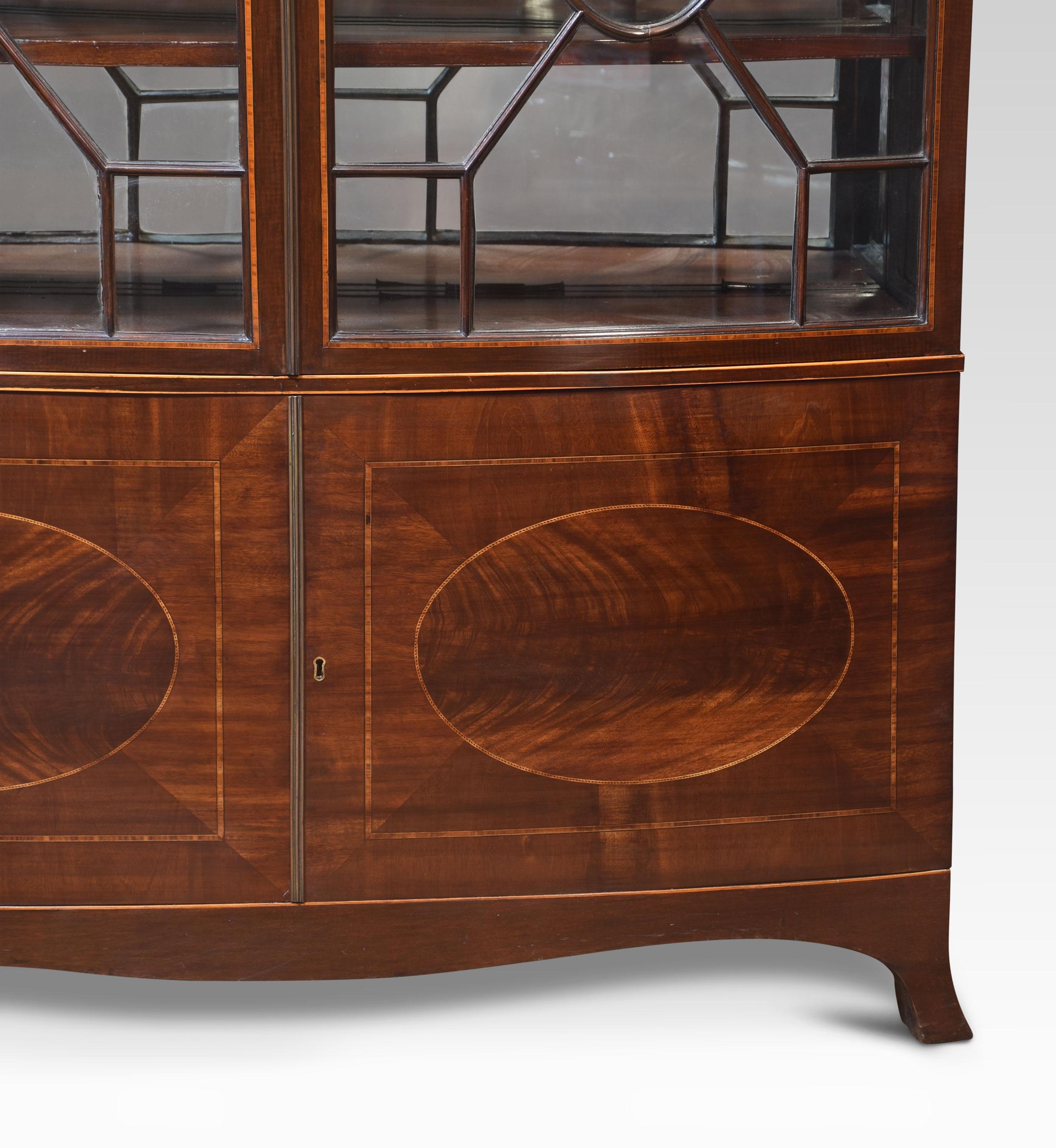 Mahogany bow front display cabinet. The shaped moulded carved cornice above a pair of astragal glazed doors enclosing unusual mirrored back and shelved interior. The base section is fitted with a pair of doors having oval detail to the centre. All