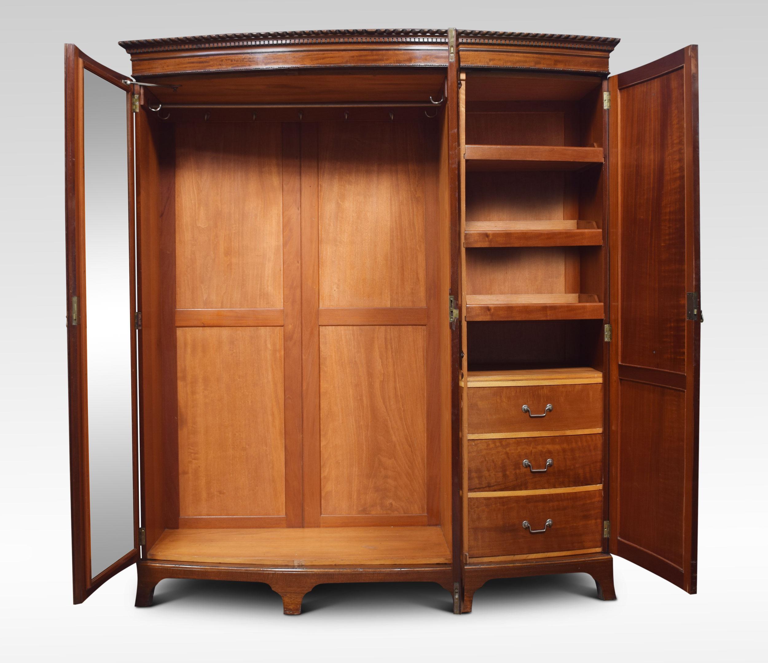 Mahogany bow fronted compactum wardrobe, the carved moulded cornice above three long paneled doors opening to reveal a fitted interior of sliding trays, draws and large hanging rail, all raised up on bracket feet.
Dimensions:
Height 82.5
