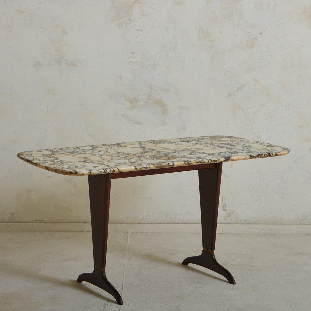 A 1970s Italian coffee table featuring a gorgeous rectangular brecciated marble top with a range of cream, taupe and chocolate hues. The tabletop has curved corners and an elegant beveled edge. This table has a carved mahogany base with patinated