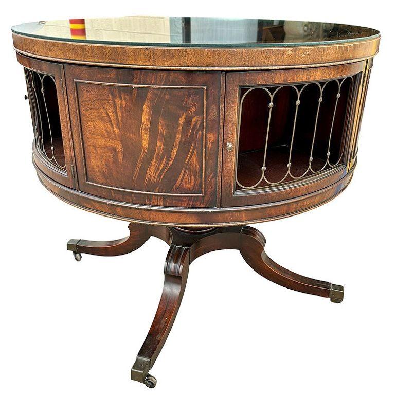Regency-styled mahogany & brass rotating round drum coffee table w/ Inlaid Leather signed by Weim. The table features 4 doors that open to one compartment for storage which can rotated on top of the 4 leg base. Each door features a solid brass grill