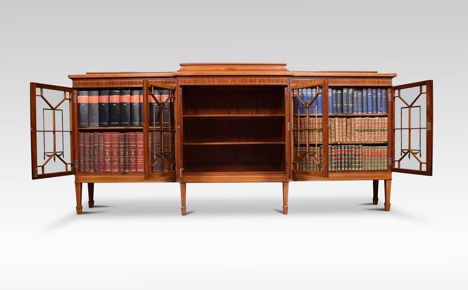 Mahogany breakfront glazed bookcase, the top with raised gallery, above two large central oval well figured inlaid panel doors, opening to reveal shelved interior. Flanked by glazed beaded doors opening to reveal two adjustable shelves. All raised
