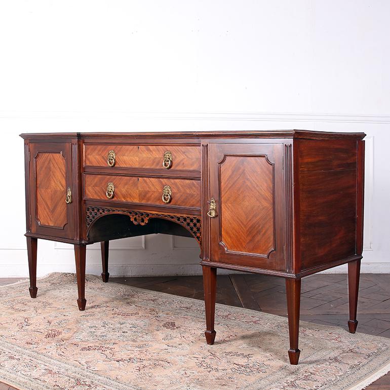 An English, Mahogany, breakfront sideboard fitted with original hardware, and having two central drawers over a curved fretwork apron, flanked by cupboards with paneled doors, all supported on square tapered legs ending in spade feet.
Dimensions:
W: