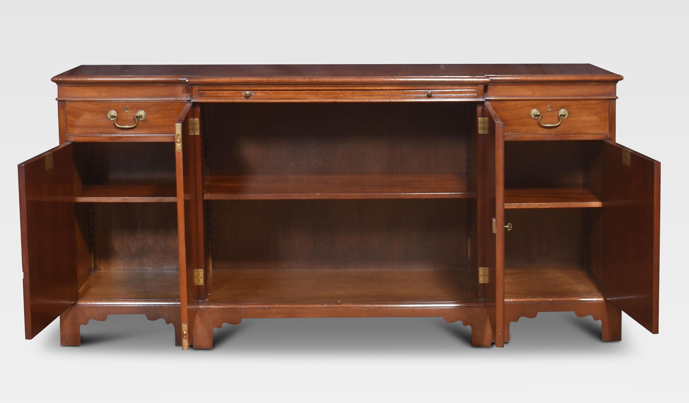 Mahogany Sideboard the long rectangular breakfront top above a central brush-in slide having two panelled doors below opening to reveal an adjustable shelf. Flanked by two banks of faux drawers, opening to reveal further shelving. All raised on