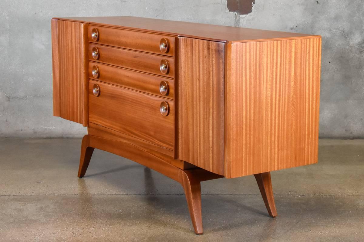Gorgeous early 1940s buffet by modern pioneer, Gilbert Rohde (1894–1944), for Brown Saltman. Constructed in beautiful golden mahogany with fantastic details in the pulls and along the front edge. The piece has plenty of storage between three