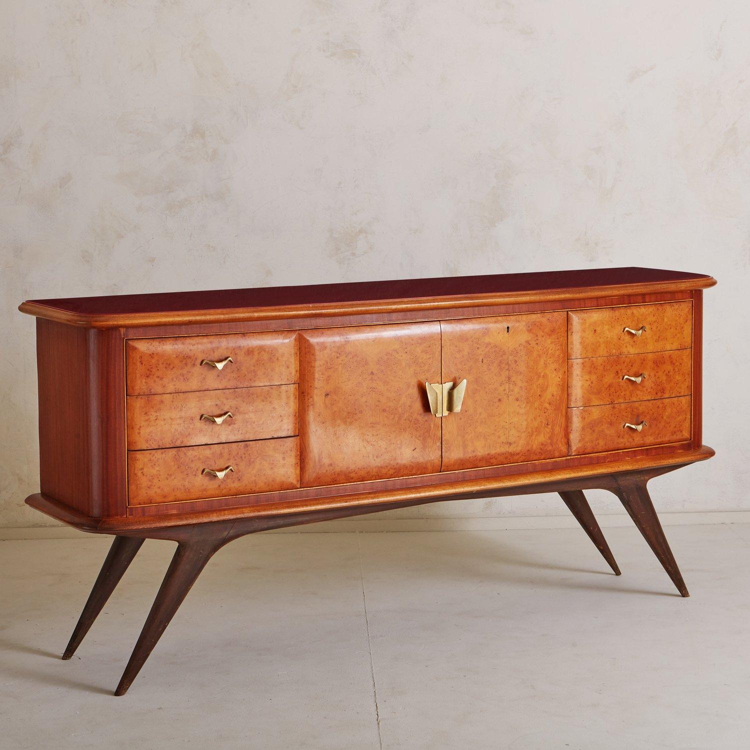 A stunning Italian mahogany and burlwood credenza with a vibrant red glass top. This piece has six drawers and two center doors which open to reveal an antiqued mirror interior and one shelf. It has beautiful patinated brass hardware and stands on