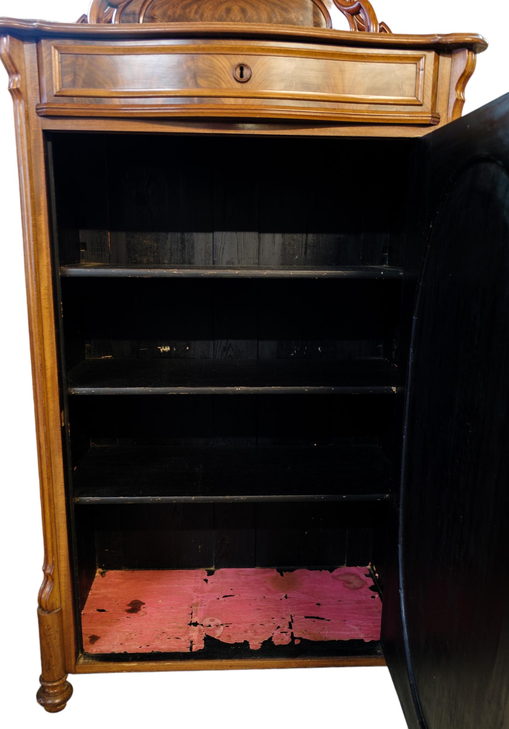 Mahogany cabinet with door and 3 shelves decorated with wood carvings and intarsia from around the 1880s.
Measurements in cm: H:175 W:88 D:46