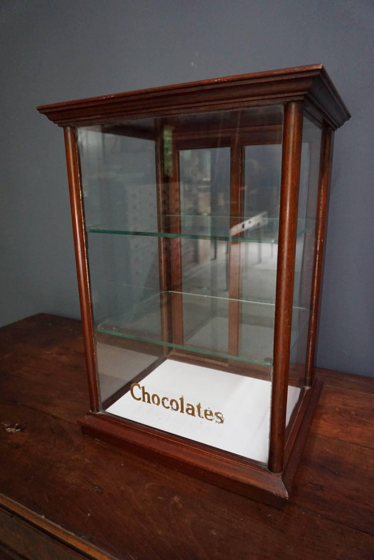 This shop display cabinet is made from mahogany, the glass has gold leaf lettering on the front of the cabinet saying Cadbury’s at the top (missing but still visible in the glass) and chocolates at the bottom. The cabinet has two sliding doors at