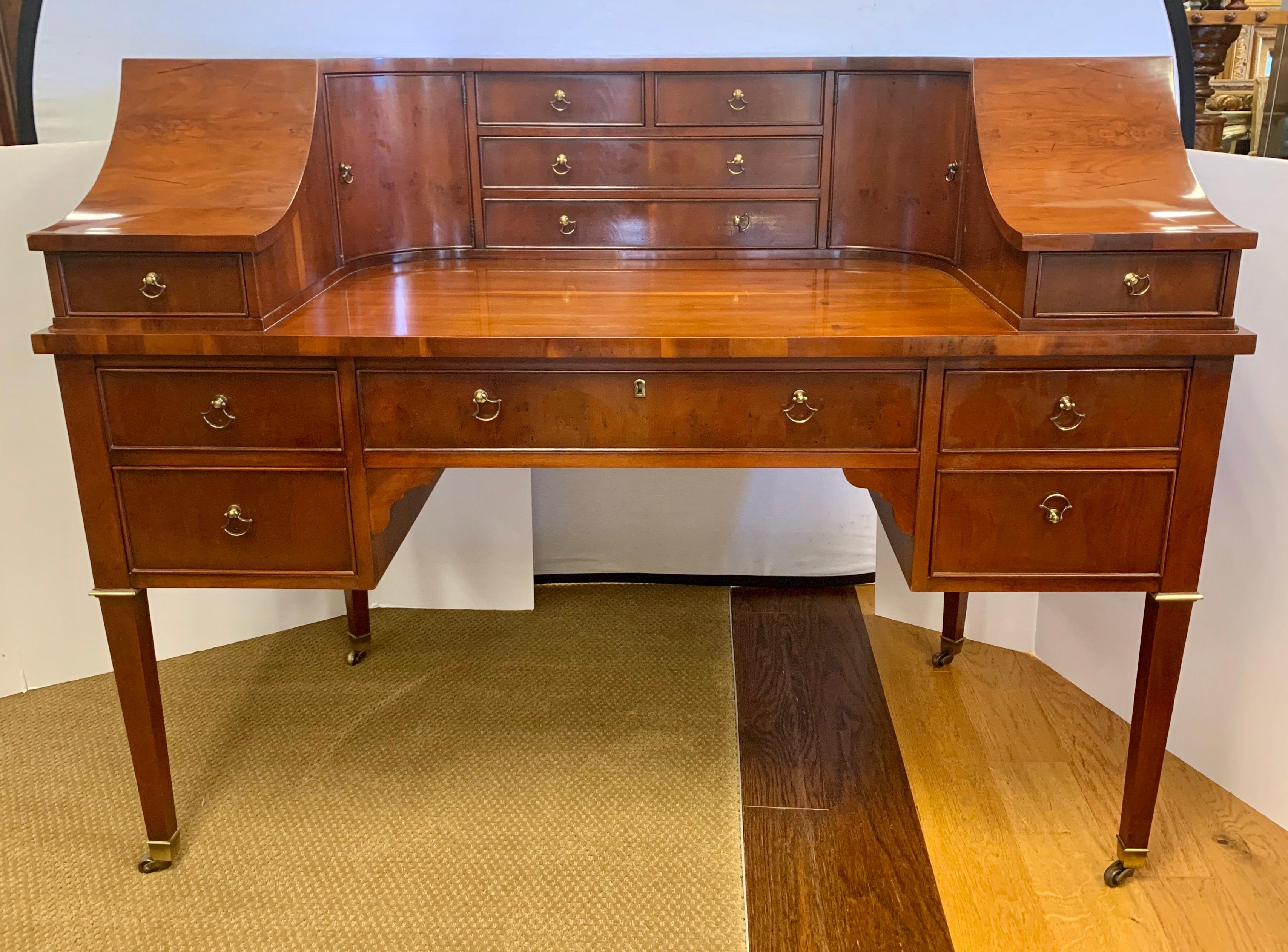 High quality and excellent craftsmanship define this Carlton house writing desk. It has a shaped top over a writing surface with multiple dovetailed drawers and cupboards. It is raised on square tapering legs, terminating in brass castors for ease
