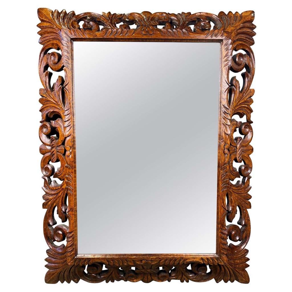Extravagantly carved mahogany mirror in rectangular dimension. A lovely grain pattern runs symmetrically across the wood surrounding a very generously sized fitted mirror.
