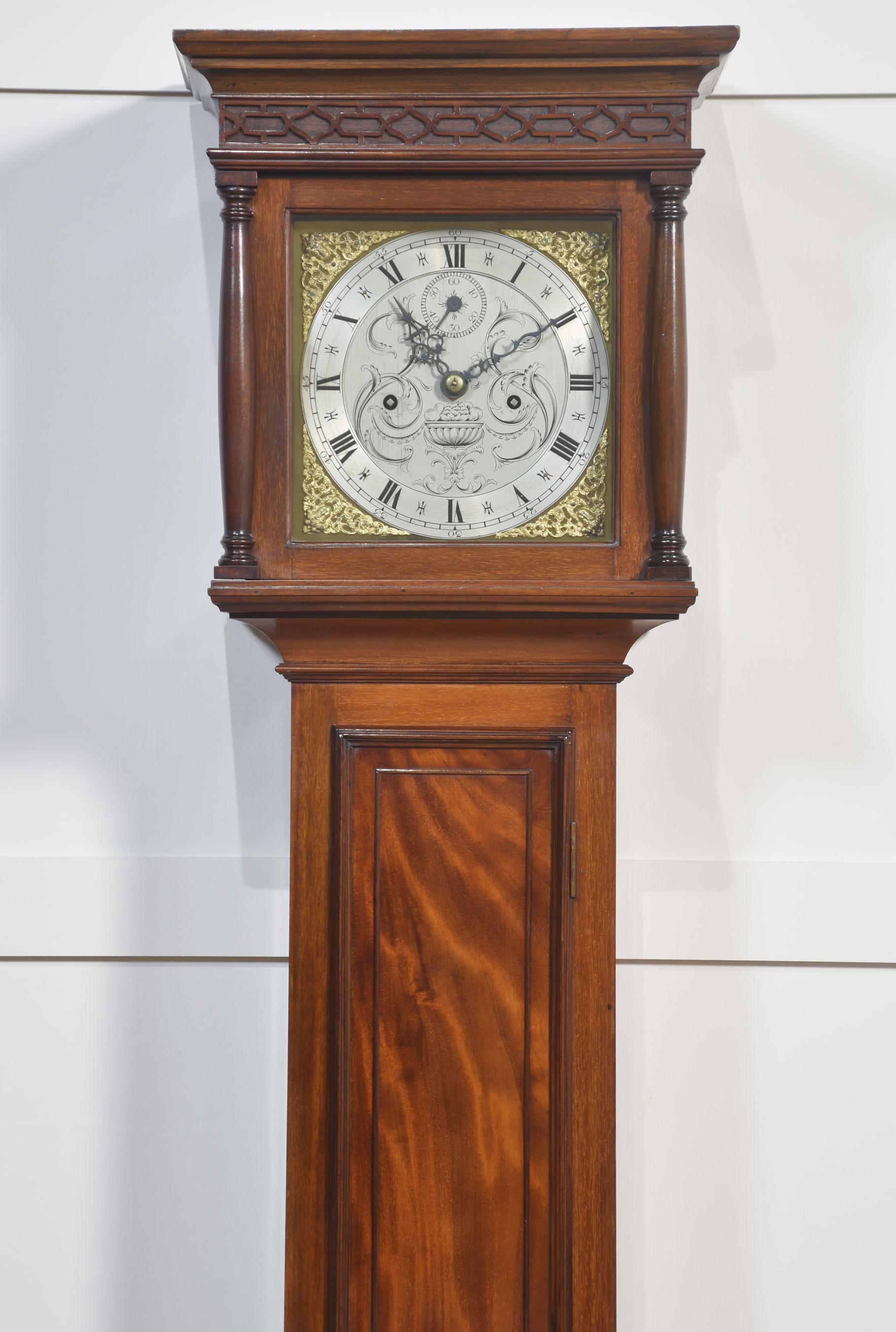 Orologio da nonna con cassa in mogano, cappuccio sagomato e quadrante in ottone inciso con numeri romani in metallo dorato e quadrante decorato con foglie. Il movimento a peso di otto giorni suona su un gong. La cassa in mogano ha una lunga porta