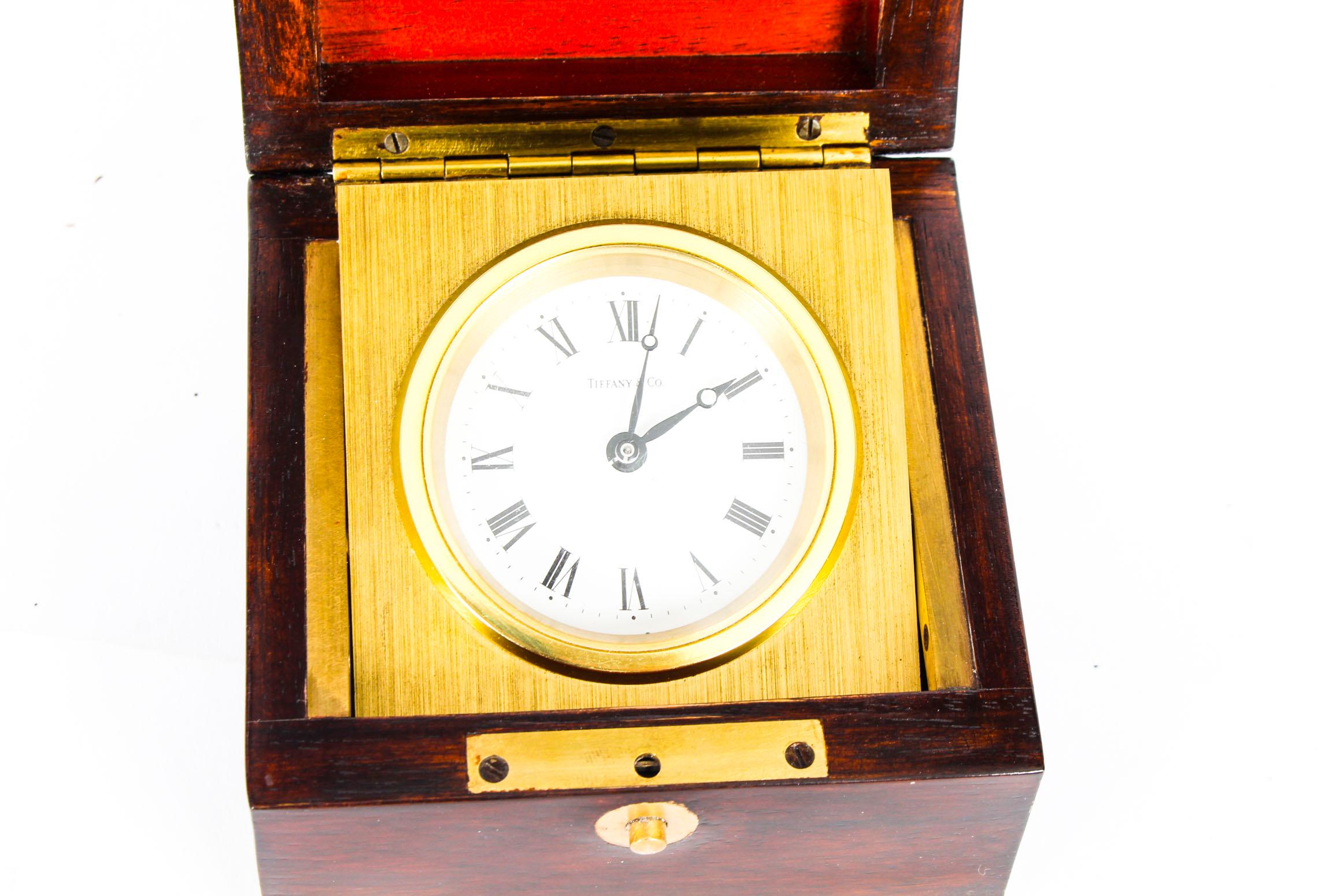 This is a elegant mahogany cased travel clock by the renowned manufacturer and retailer, Tiffany & Co, circa 1950s in date.

The brass-mounted casket opens up to reveal a brushed brass swing case framing a round white enameled dial with black