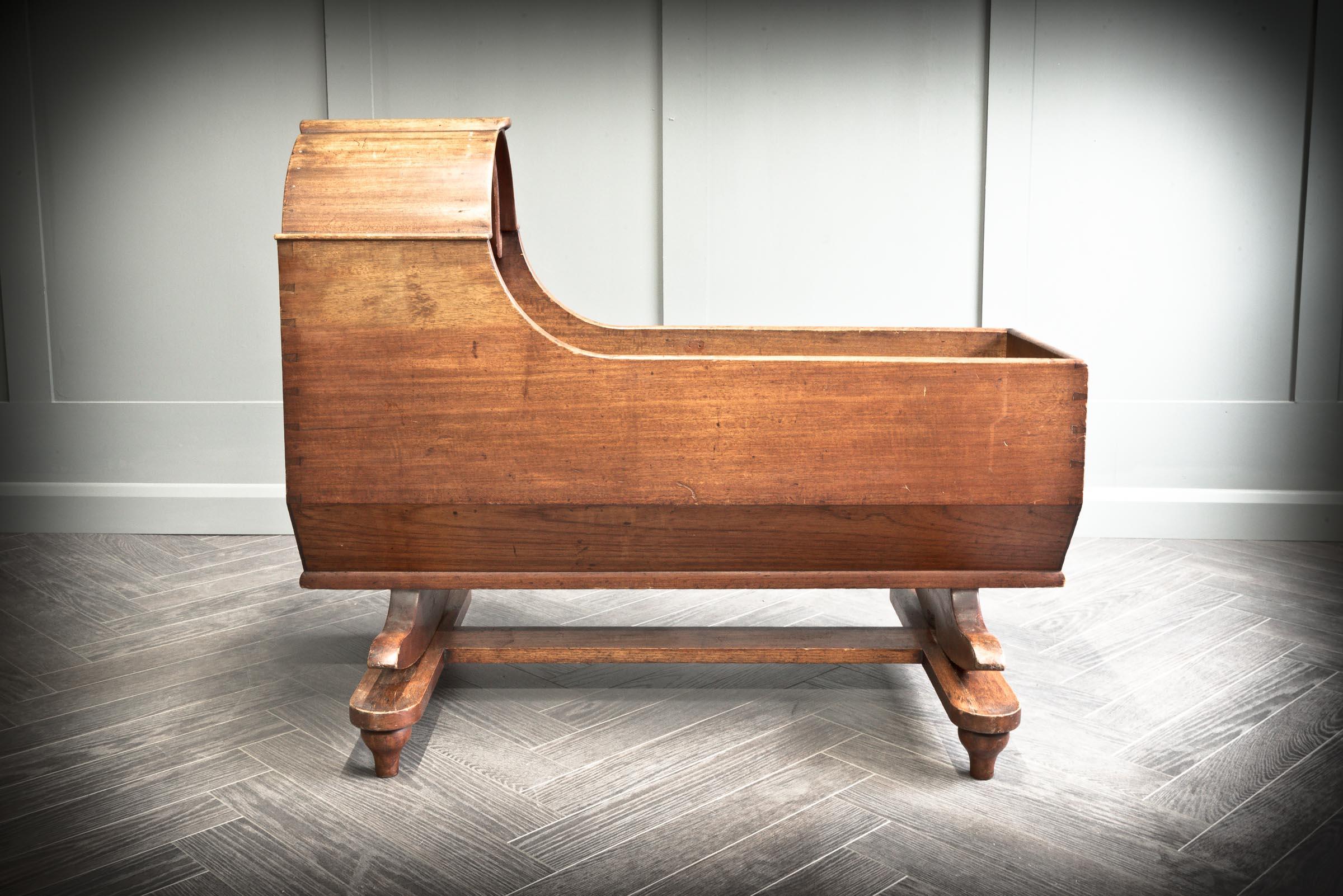 Solid mahogany childs cradle with hood. The cradle sits on a flat base and has two curved feet which allows the cradle to rock back side to side. This cradle is typical of the Victorian period with a beautiful natural grain to the mahogany.