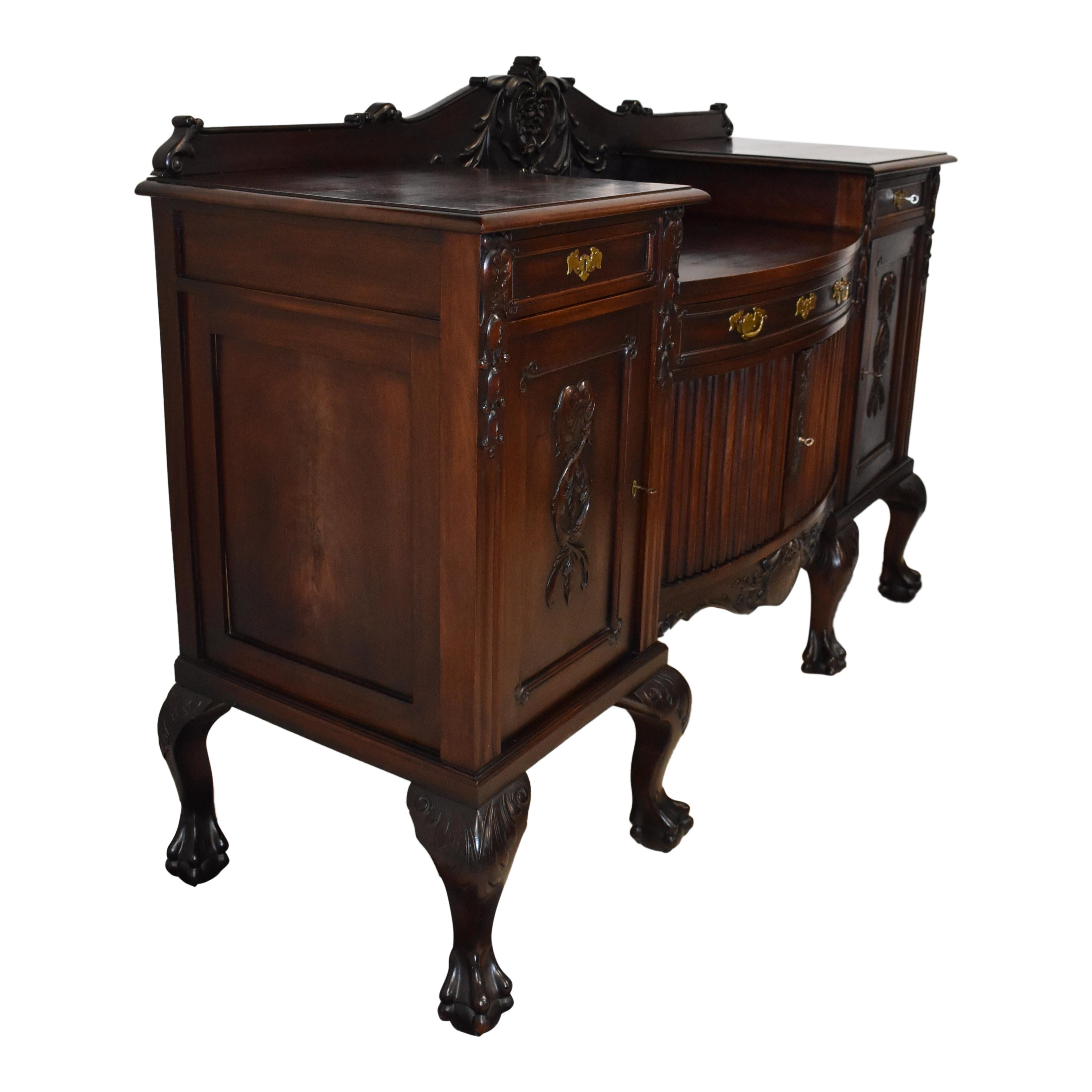 This magnificent mahogany sideboard features a drop-center with a drawer over bowed and fluted center doors flanked by side doors with carved pendant shells amid descending scrolled vines. The side doors have drawers above them, and the doors open