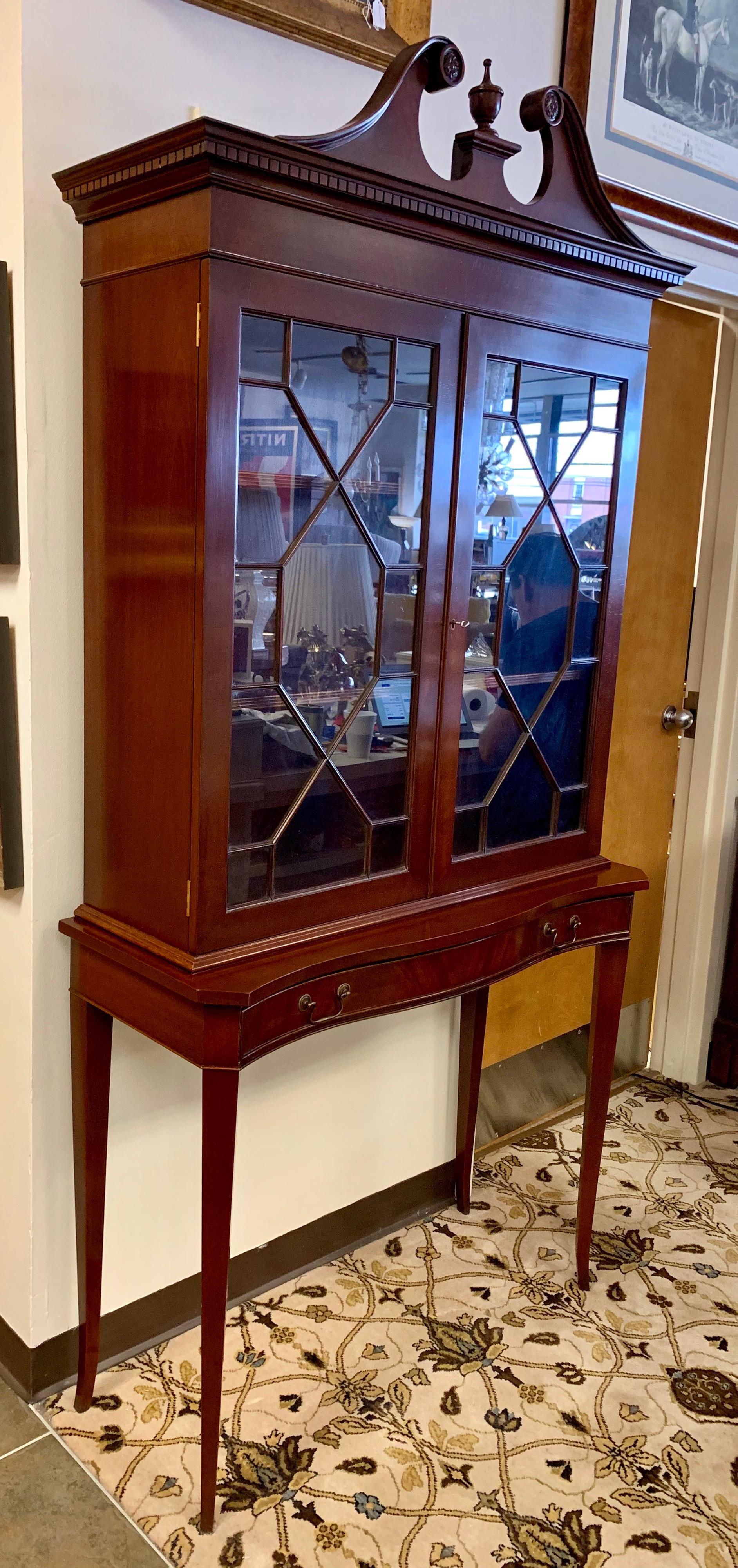 Elegant mahogany Chippendale style display library bookcase that features a large center drawer underneath a glass and mahogany enclosed cabinet. The top is lockable and the key is present.
There are two wooden shelves at top which are adjustable.