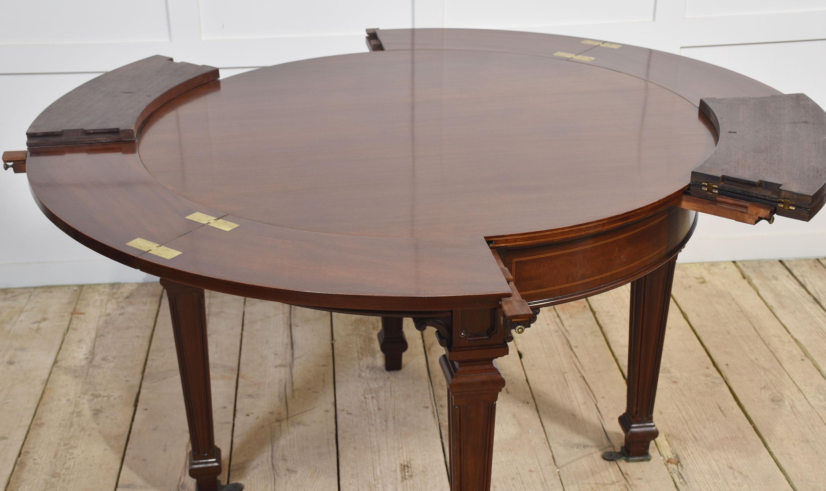 Mahogany inlaid ships dining table, the unusual circular top having four convexed drawers which open to reveal four original mahogany hinged leaves which can be incorporated into the pull-out arms to create a large circular dining surface. Raised up
