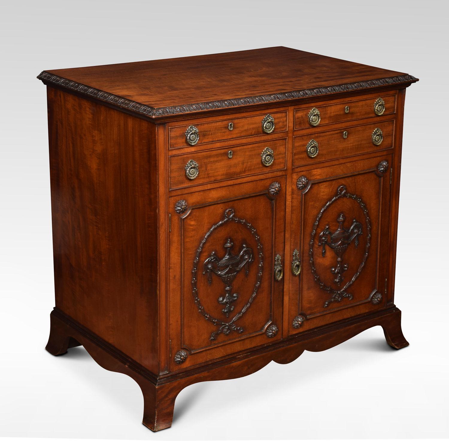 Mahogany commode in the influenced of Robert Adam, the rectangular top having carved edge above four short drawers with tooled brass handles over two doors with classical urns, ribbon and swags mouldings, opening to reveal single fixed shelf Raised