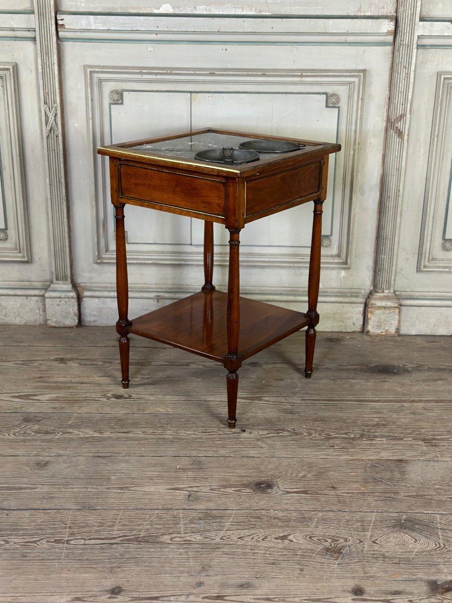 Table de rafraîchissement En acajou et placage d'acajou, plateau en marbre gris Sainte Anne équipé de deux seaux en zinc, la ceinture ouvrant à un tiroir, reposant sur des pieds fuselés réunis par une tablette d'entrejambe.